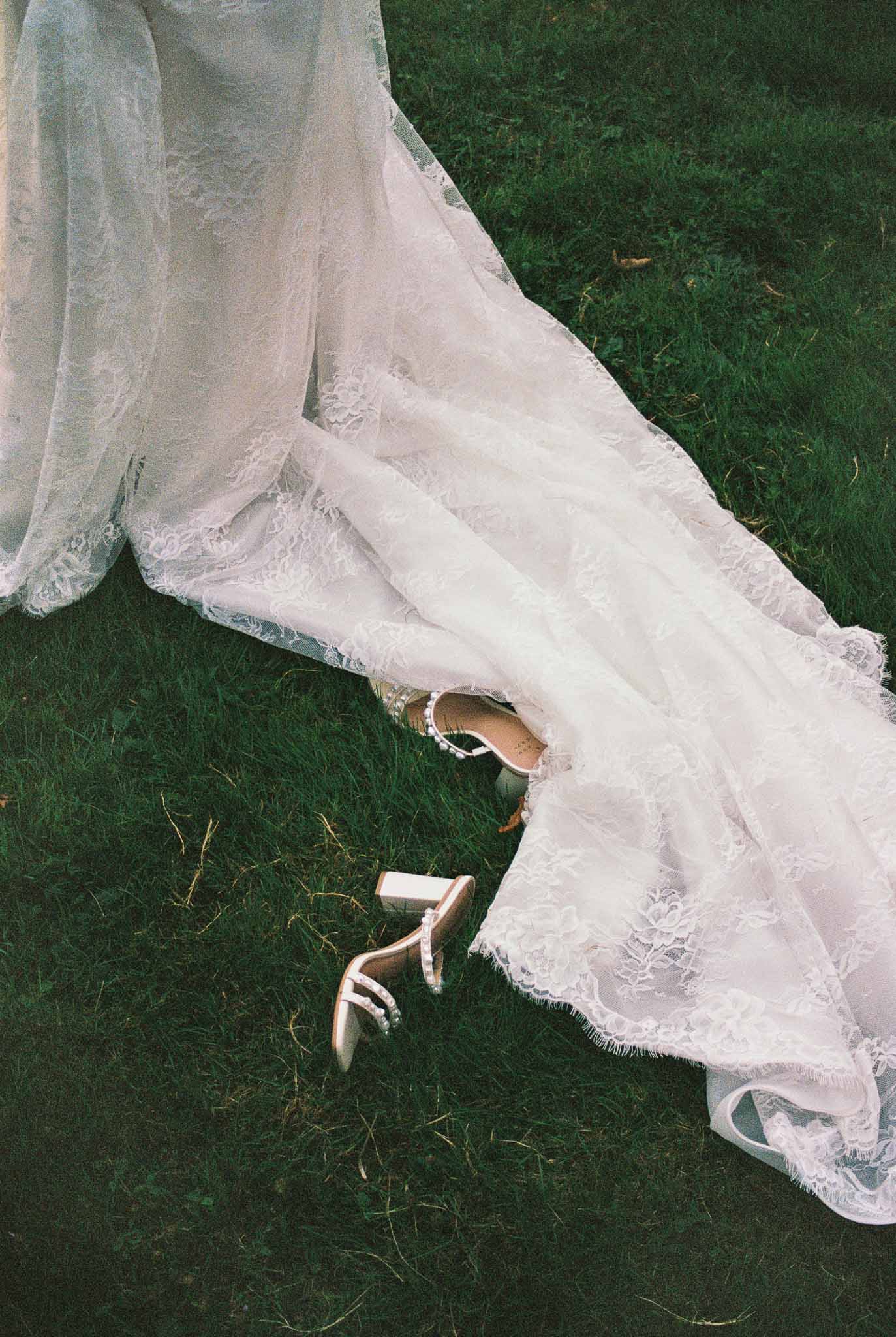 Bride's ivory lace wedding dress train on grass during outdoor portrait session