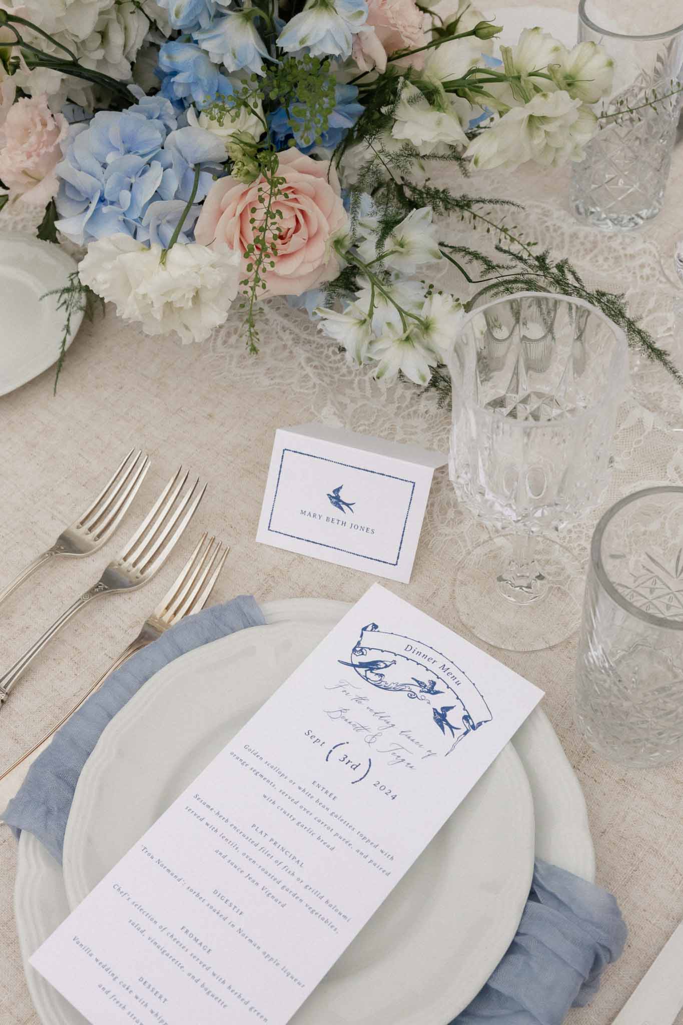 Wedding table setting with ivory plates, crystal glasses, and blue hydrangea centerpiece at elegant reception