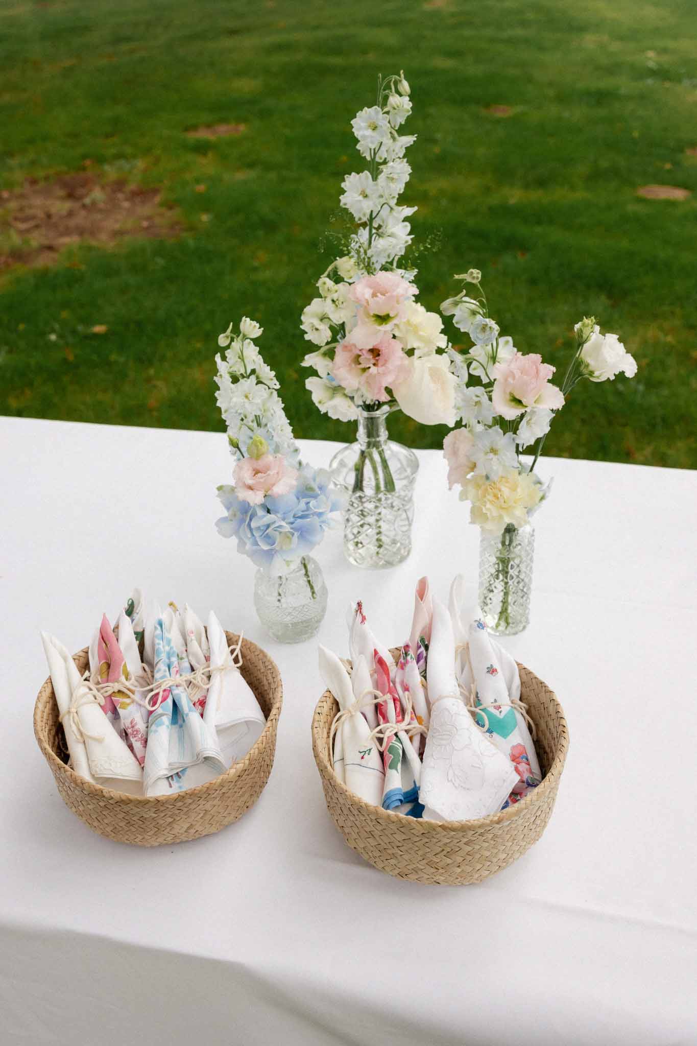 Outdoor reception table with floral centerpieces and woven napkin baskets at garden wedding venue