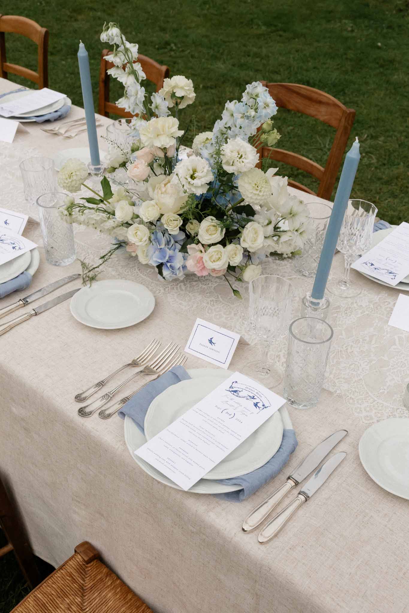 Elegant outdoor reception table setting with white floral centerpiece and blue accents in garden venue
