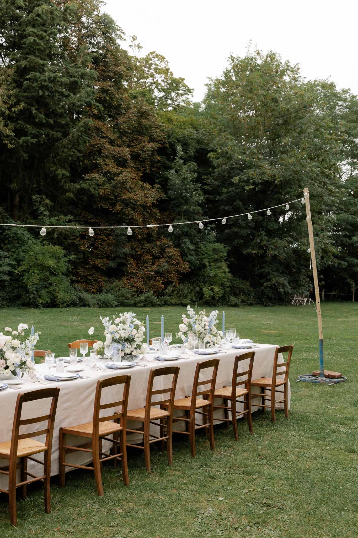 Outdoor reception table setting with white florals and string lights in garden venue