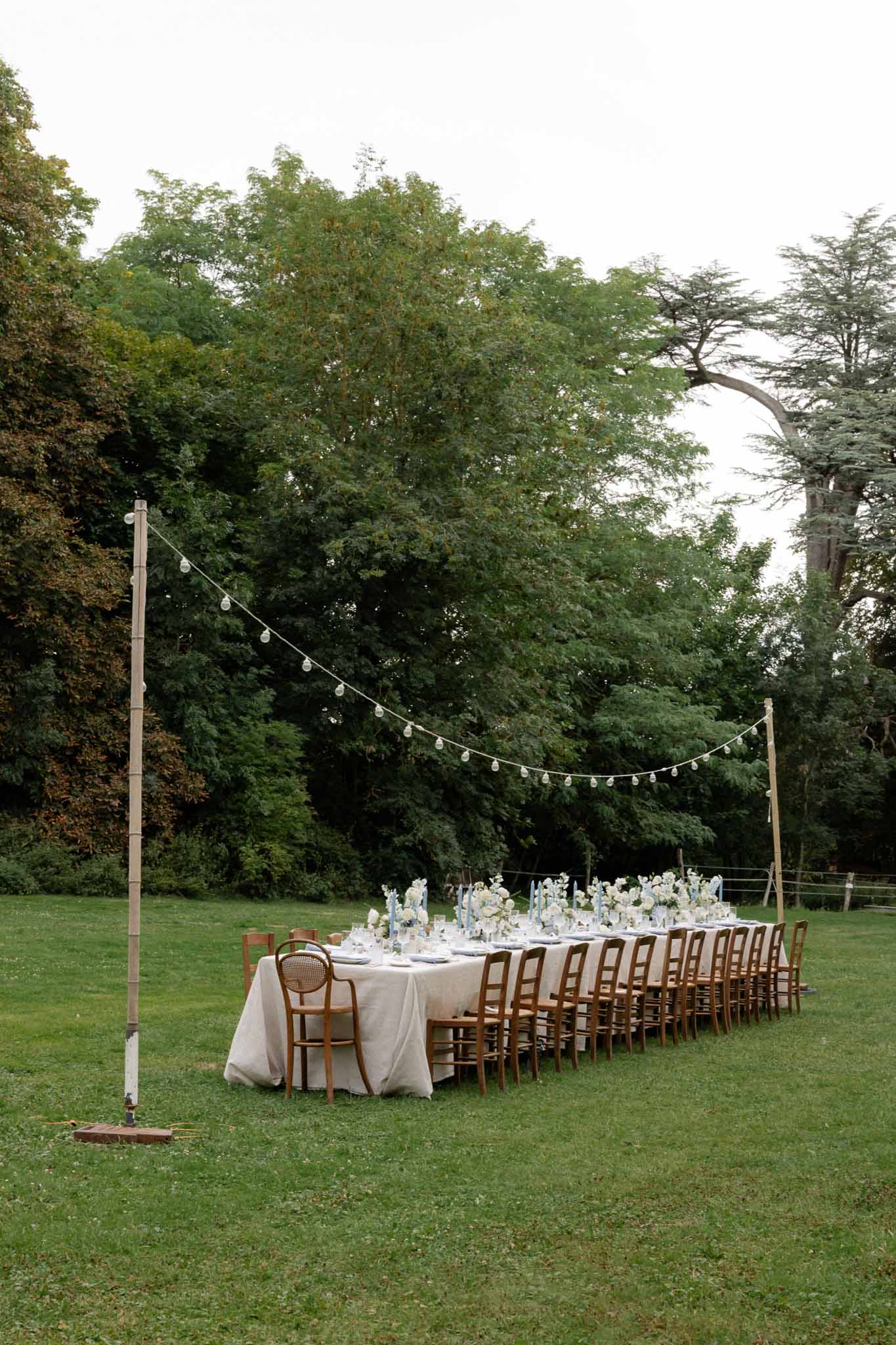 Outdoor reception table setup with string lights in wooded estate garden
