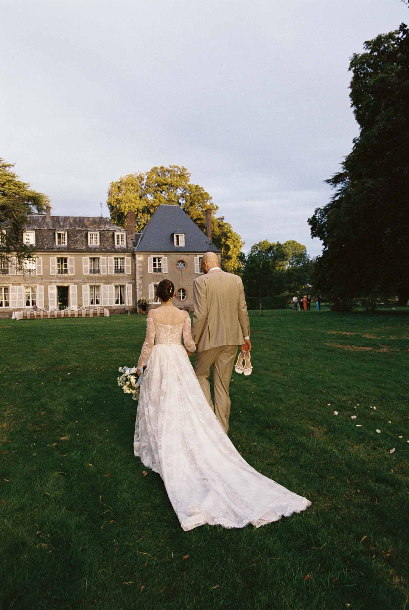 Bride and groom walking toward French château during autumn wedding reception