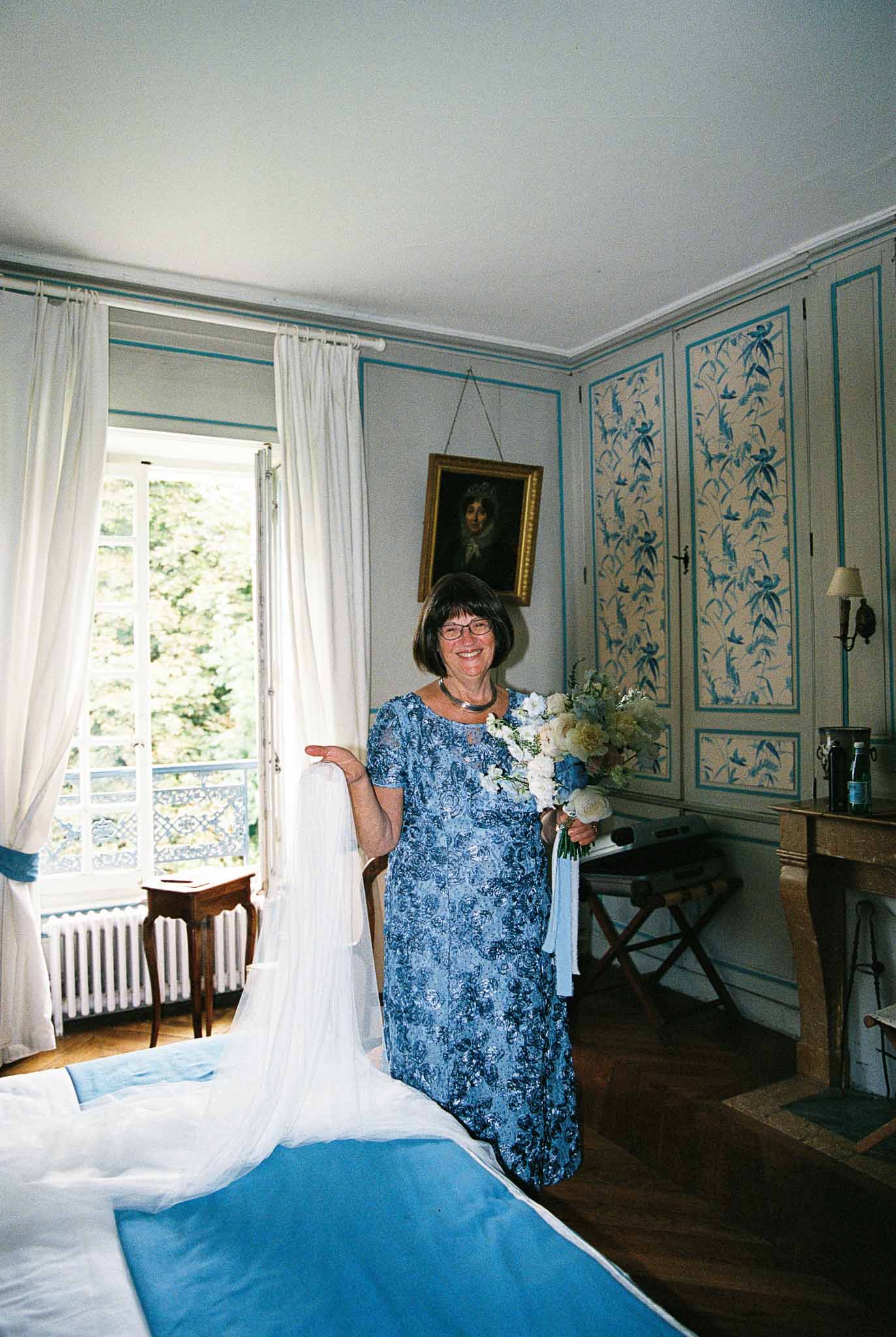 Woman in blue dress holding bridal bouquet in elegant château bedroom with teal paneled walls