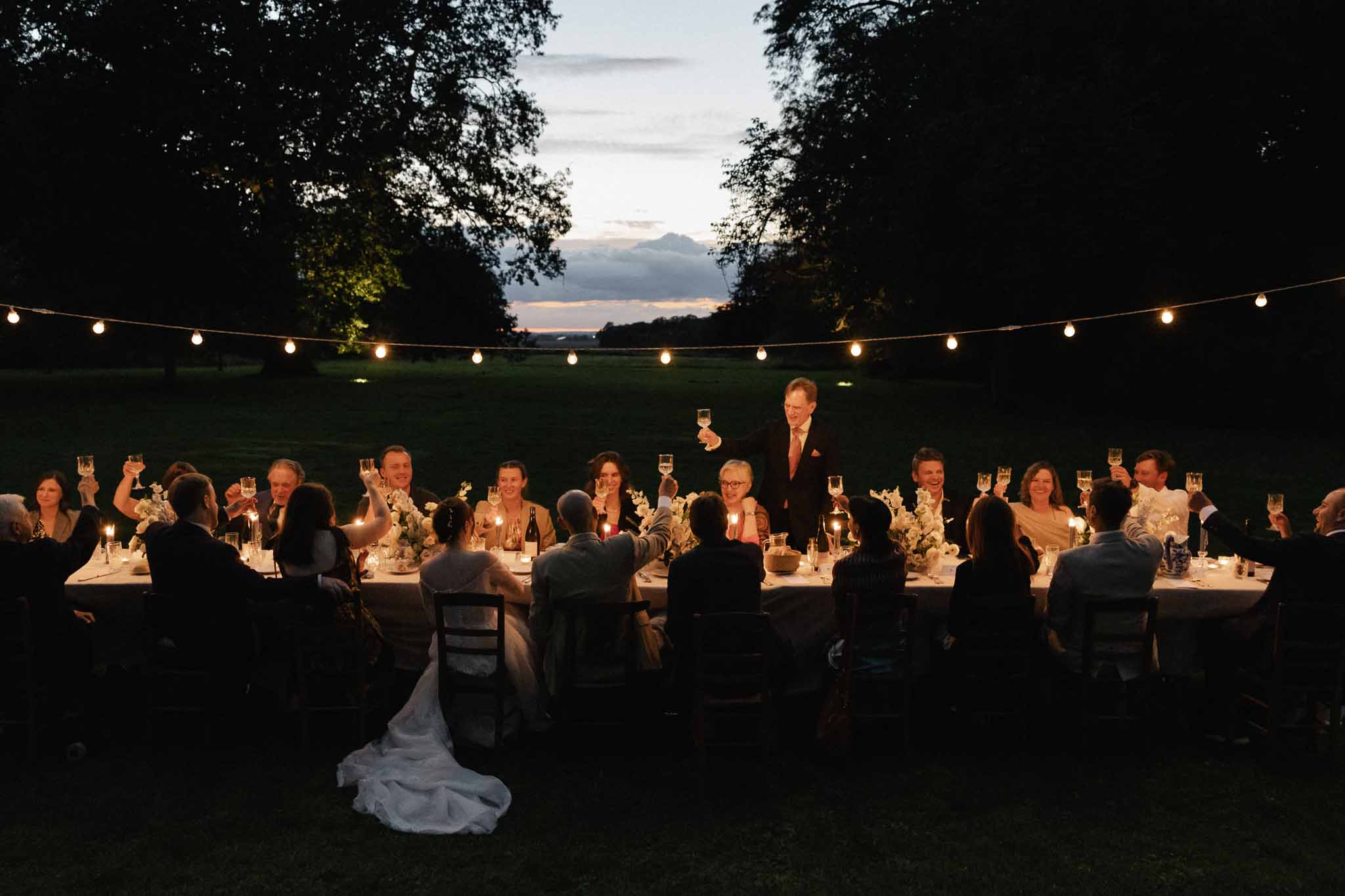 Wedding reception speech outdoors with string lights and mountain backdrop at garden venue