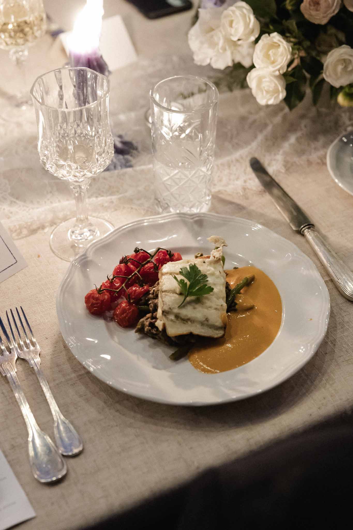 Plated dinner course with fish and crystal glasses at indoor wedding reception