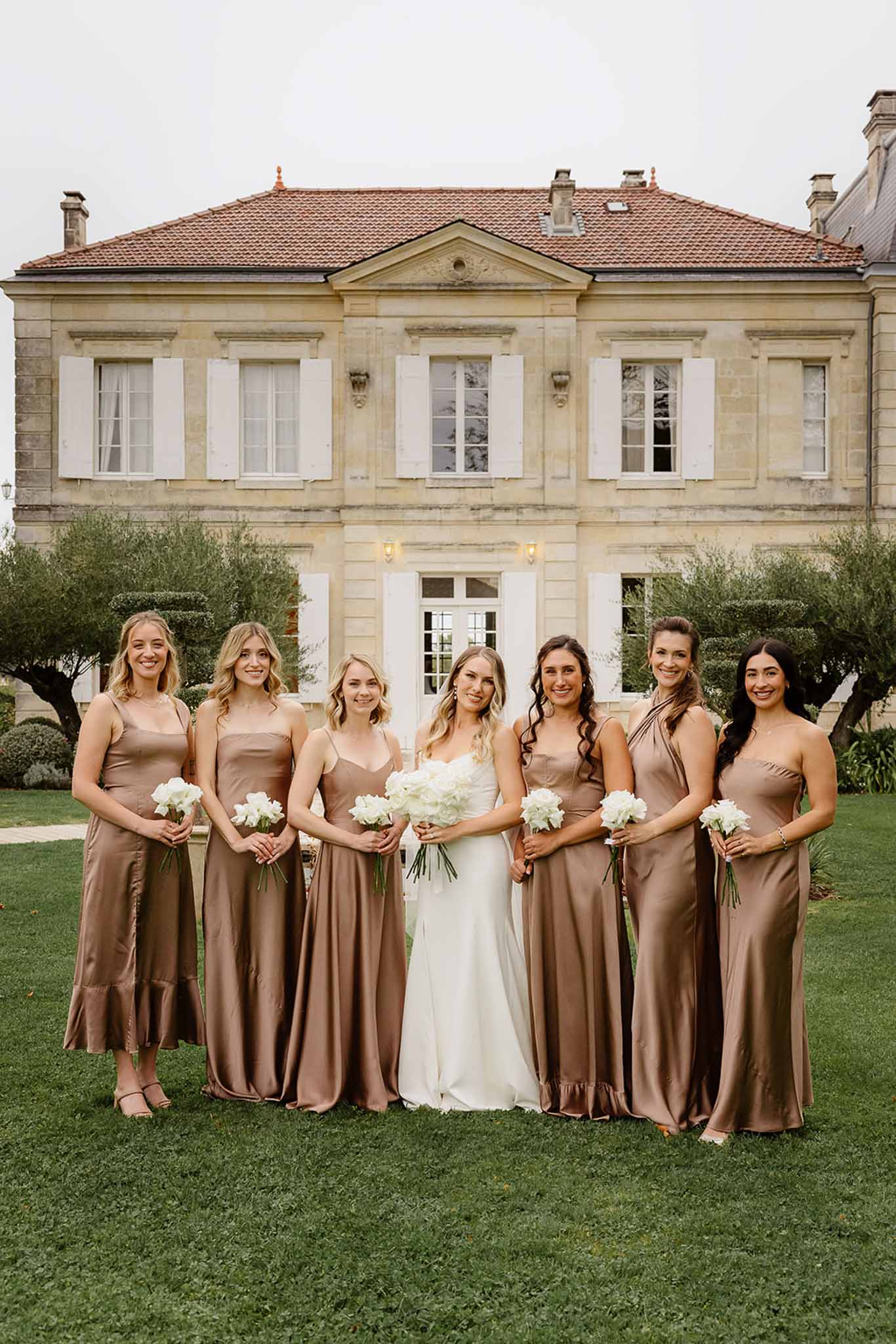 Bride and bridesmaids group portrait on lawn at stone manor house wedding venue