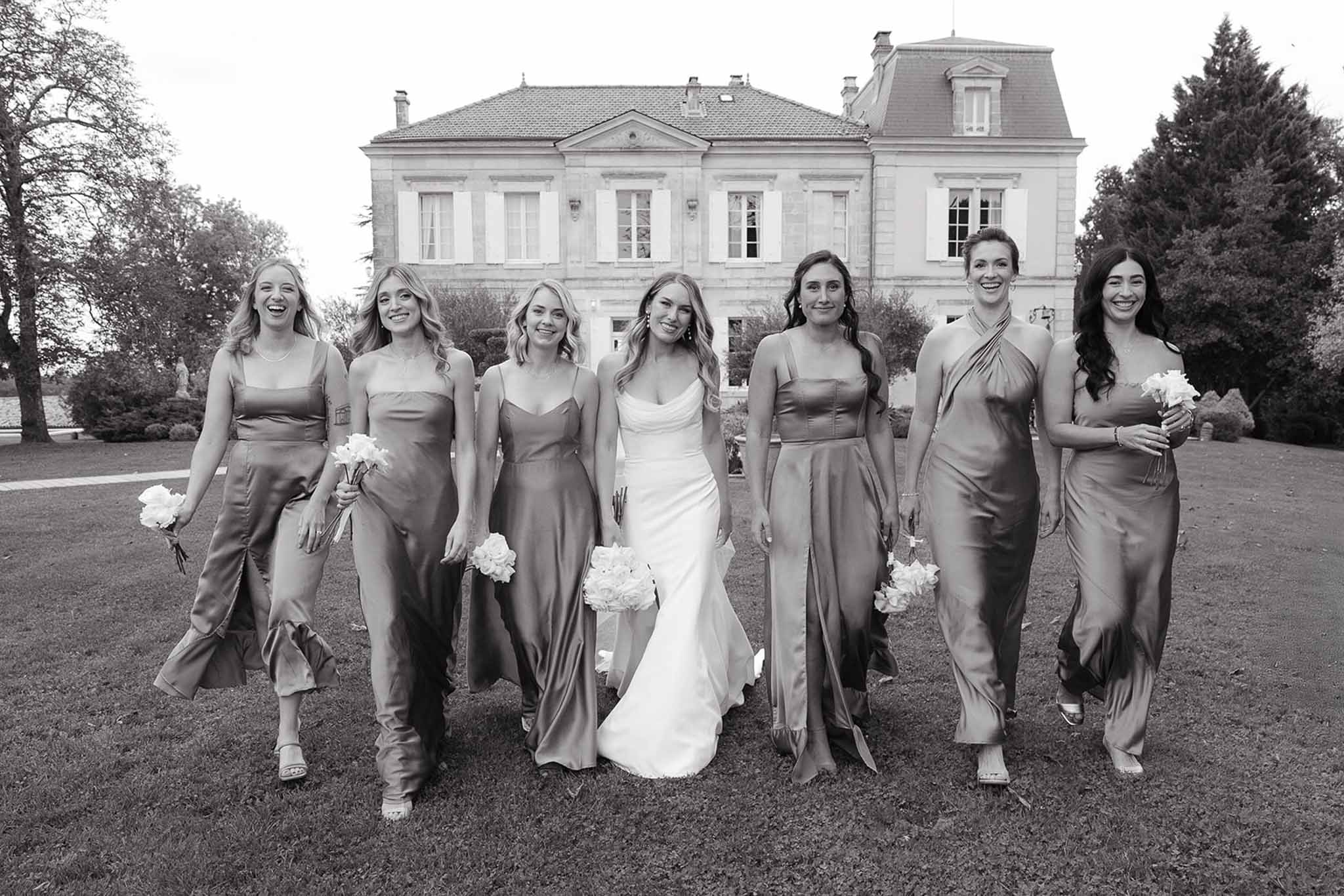Bride and bridesmaids walking toward camera at French mansion with carnation bouquets