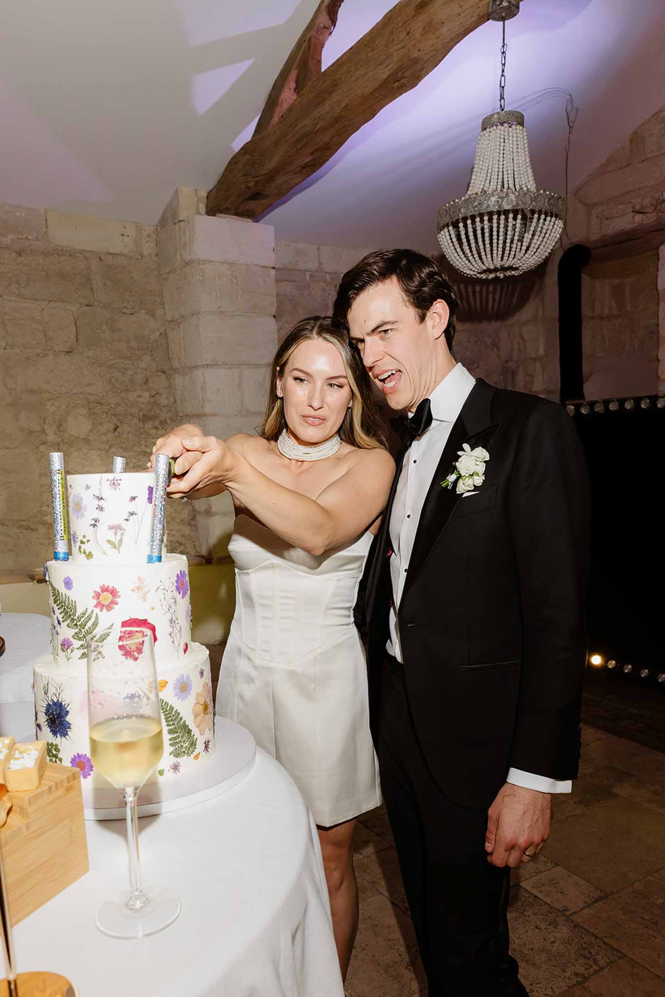Bride and groom cutting three-tiered botanical wedding cake at rustic indoor reception venue