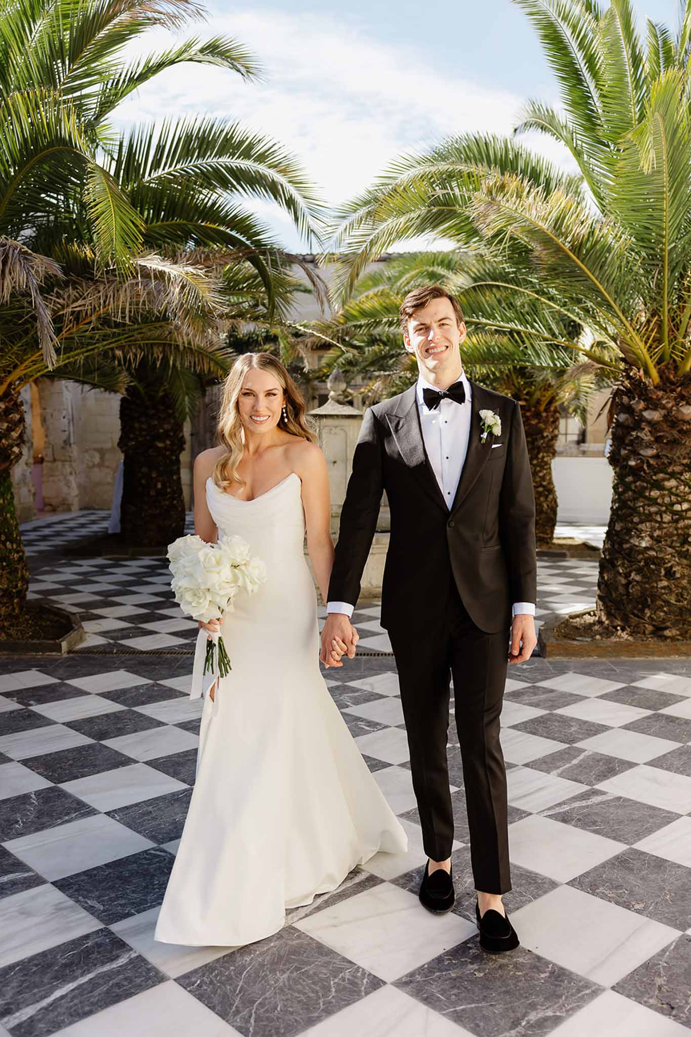 Bride and groom formal portrait in palm-lined courtyard with diamond pattern tile floor