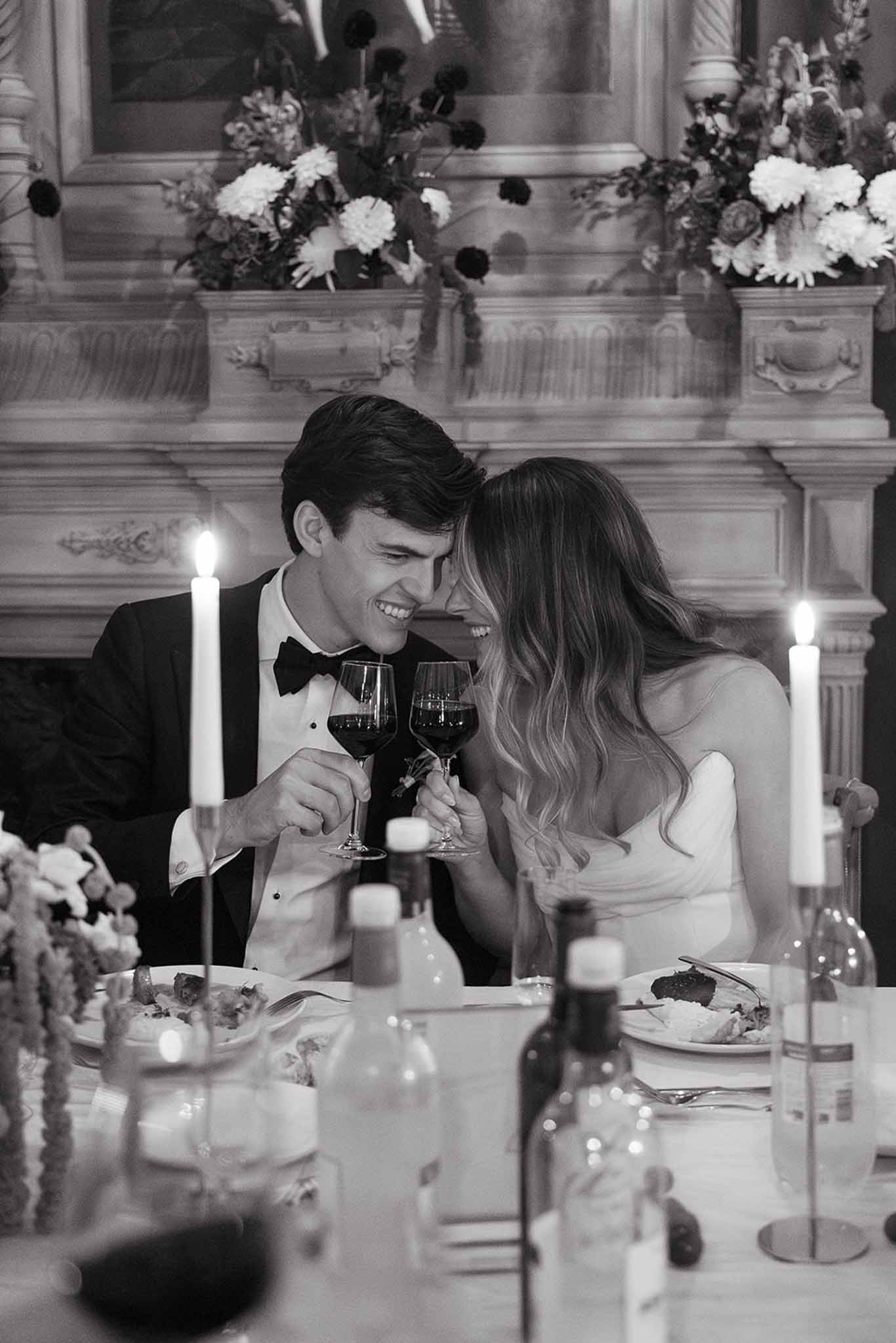 Bride and groom toasting with wine glasses at formal reception dinner table in classical ballroom