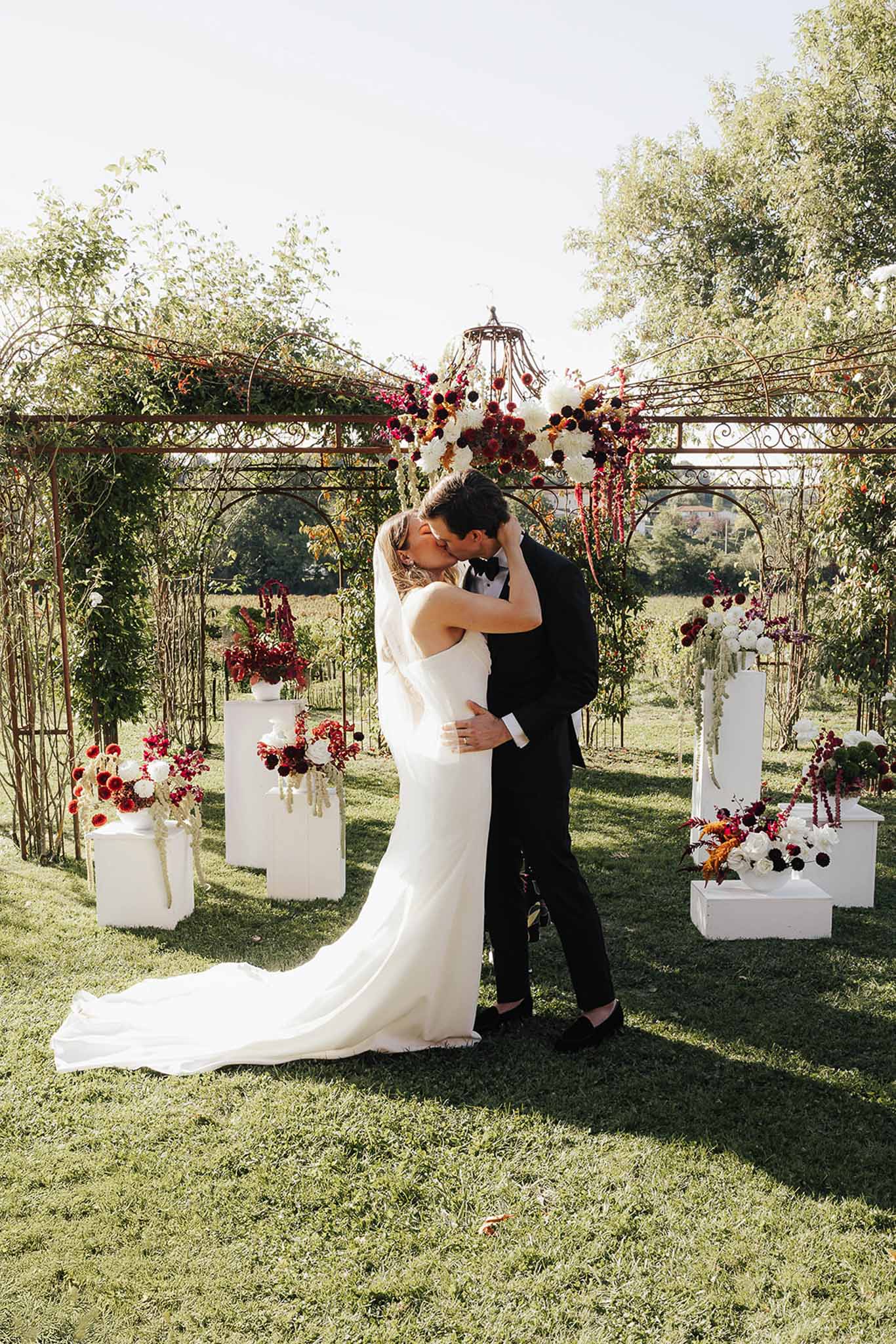 Bride and groom first kiss during outdoor garden ceremony under floral arch