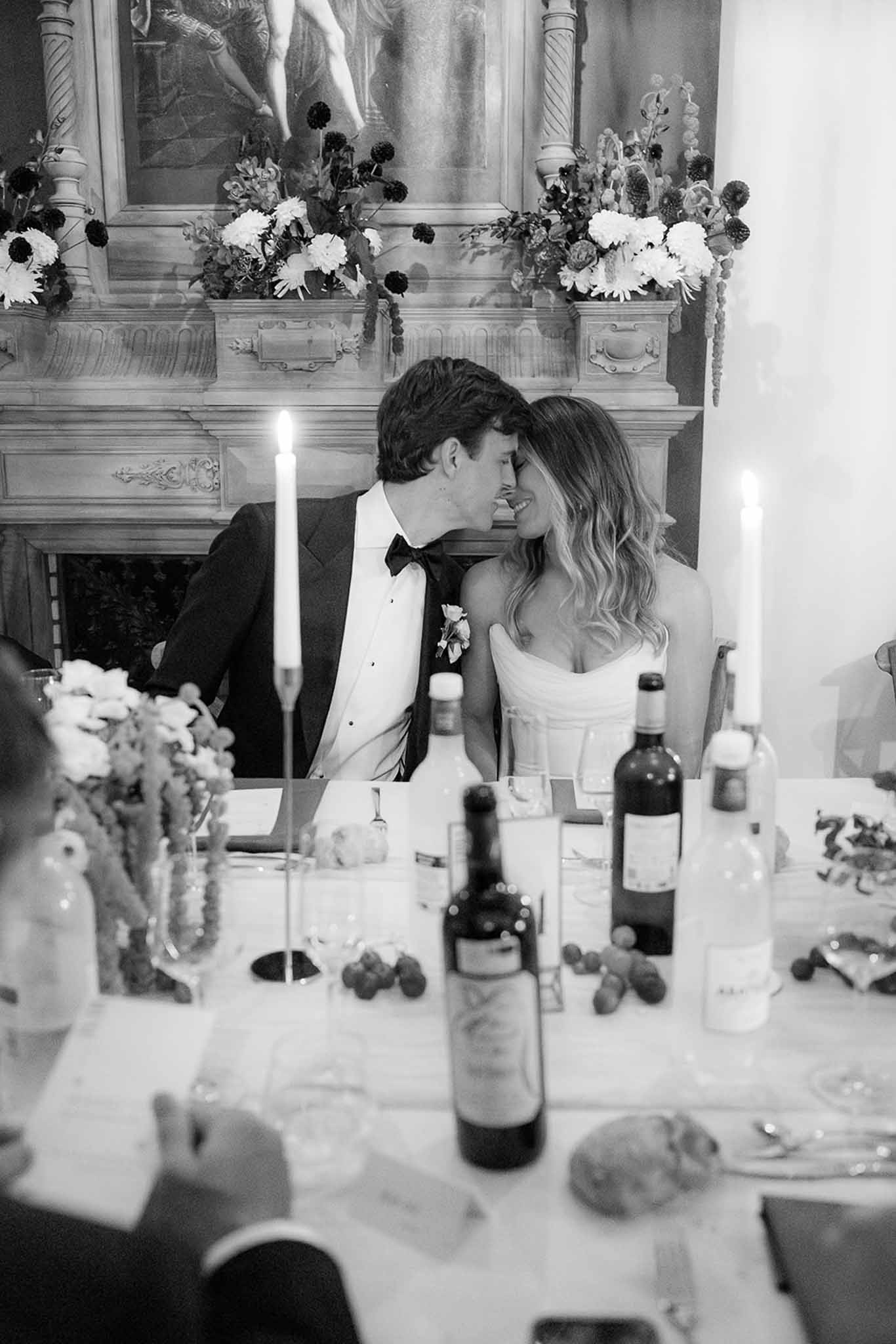 Bride and groom sharing intimate moment at reception dinner table with floral fireplace backdrop