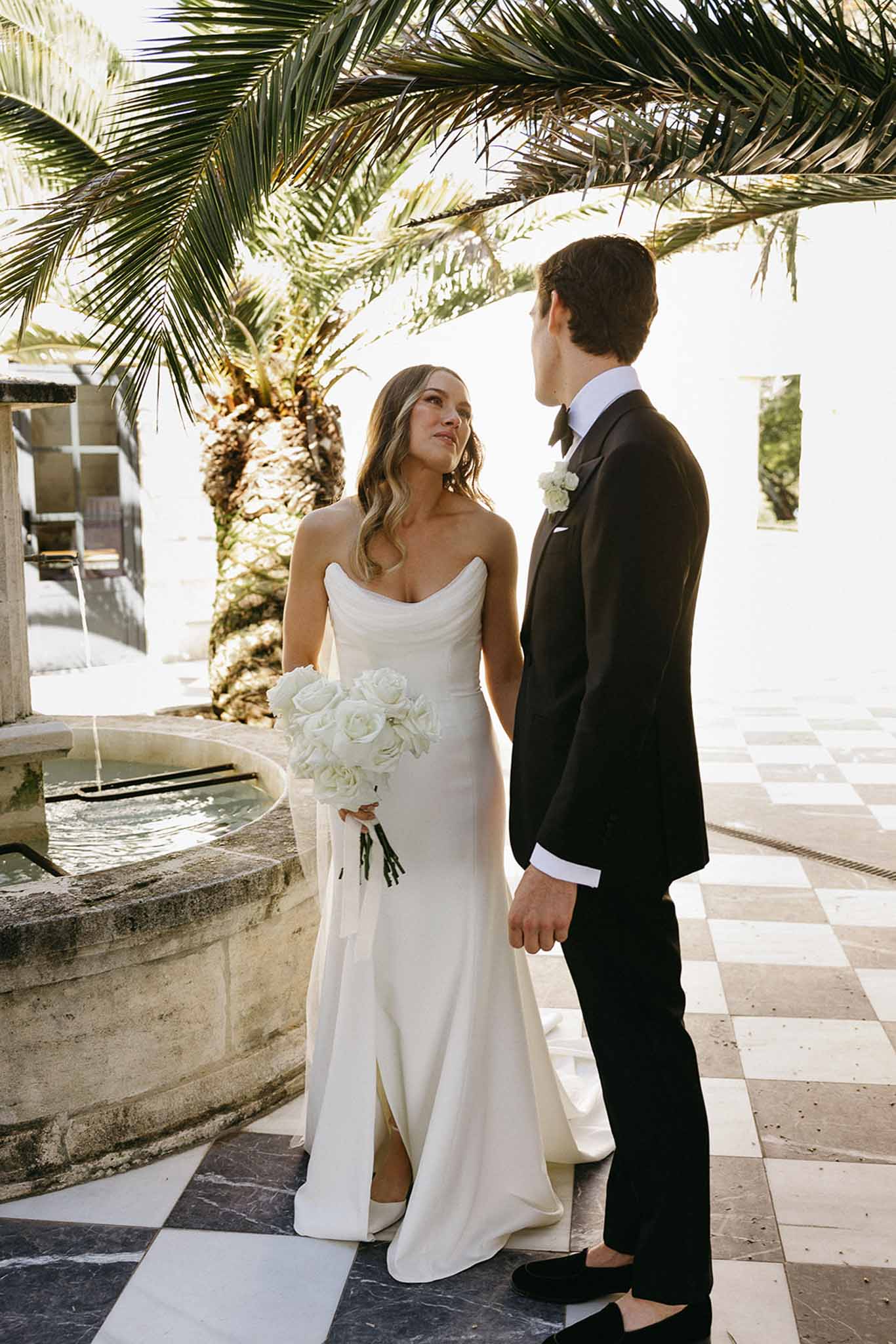 Bride and groom portrait in Mediterranean courtyard with stone fountain and palm trees
