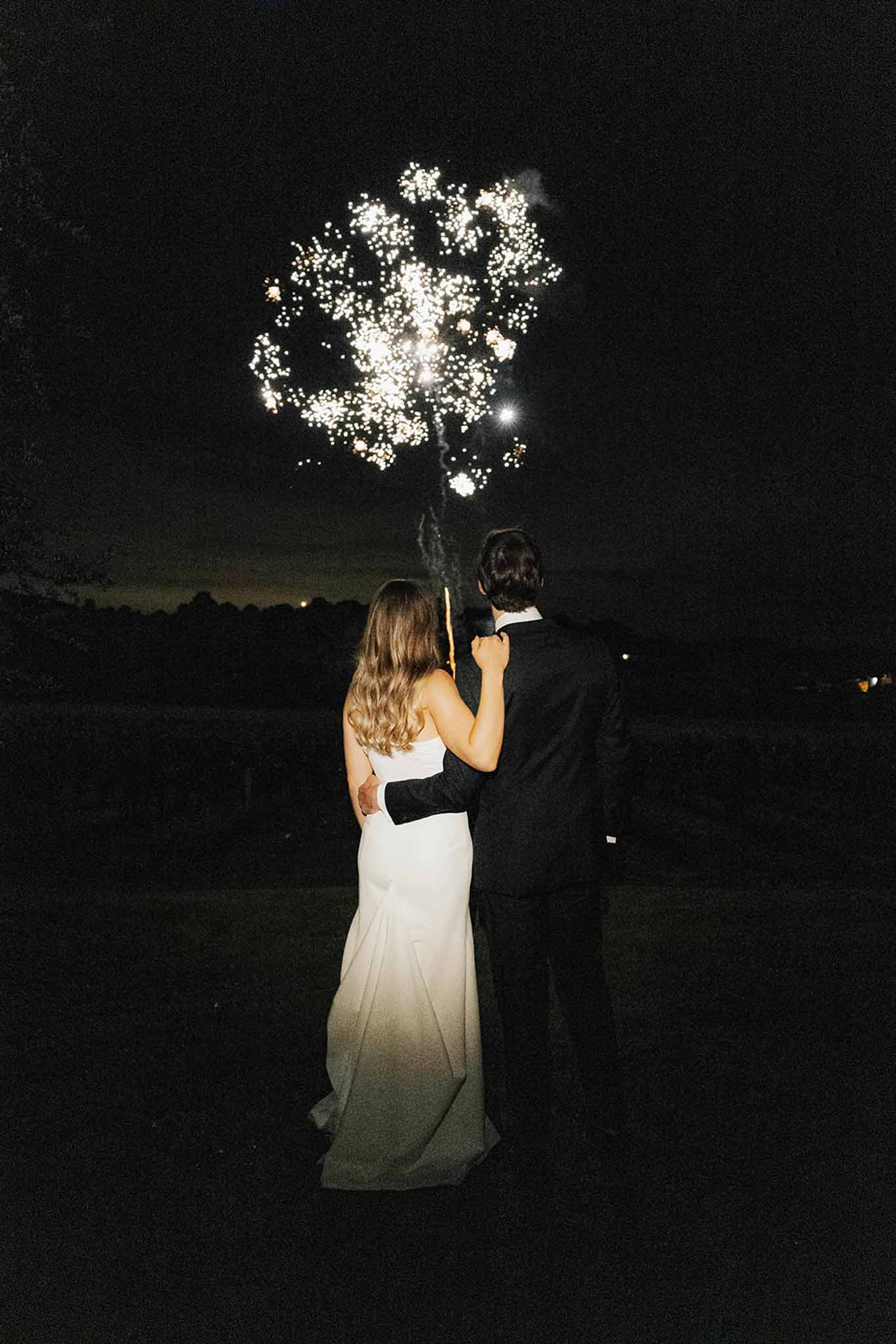 Bride and groom watching fireworks display during outdoor wedding reception finale