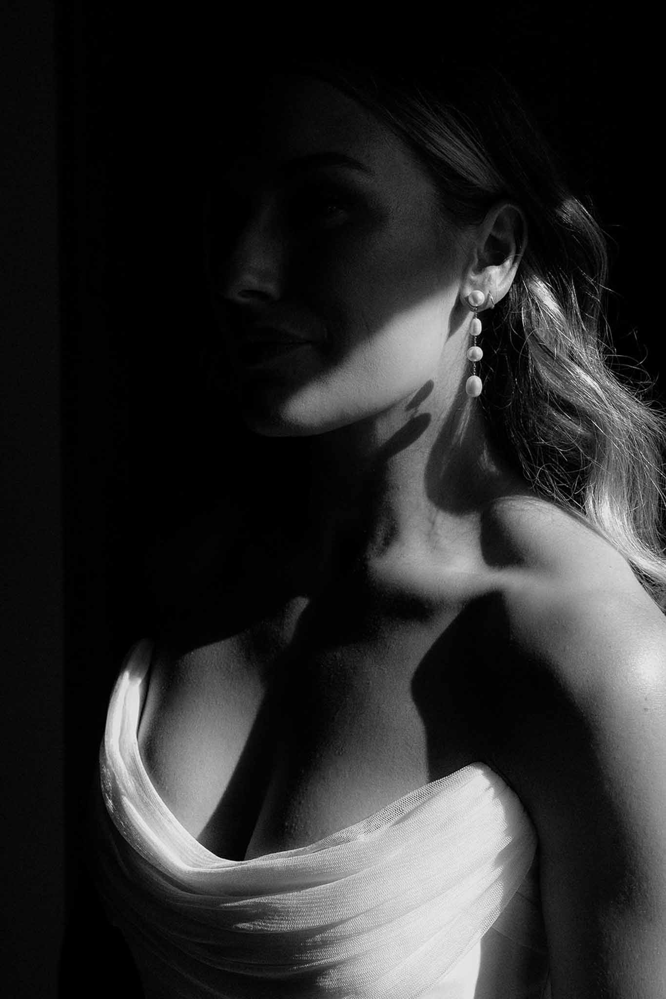 Black and white close-up portrait of bride in strapless gown with pearl drop earring and dramatic lighting