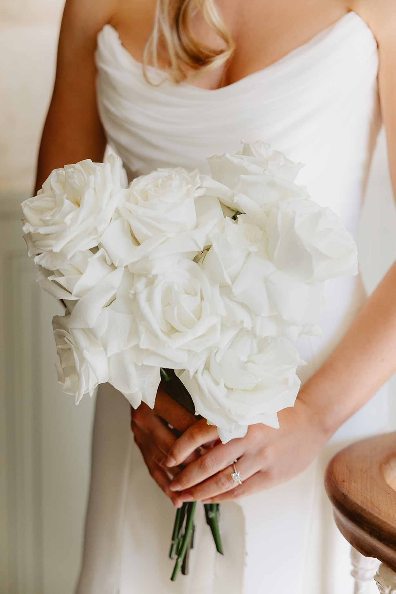 Bride holding minimal all-white rose bouquet against strapless cowl-neck gown with diamond ring visible