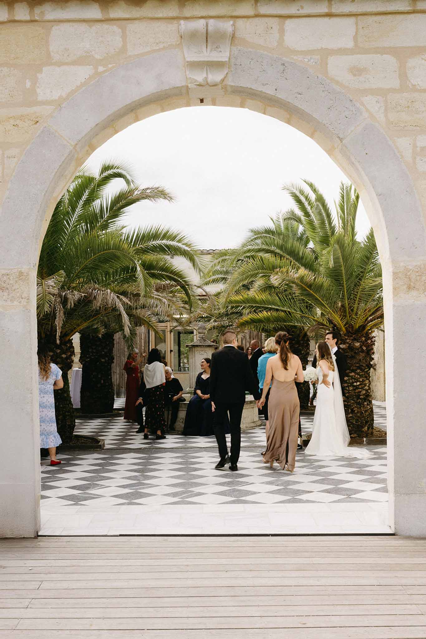 Cocktail hour guests mingling in Mediterranean courtyard with geometric floor and palm trees