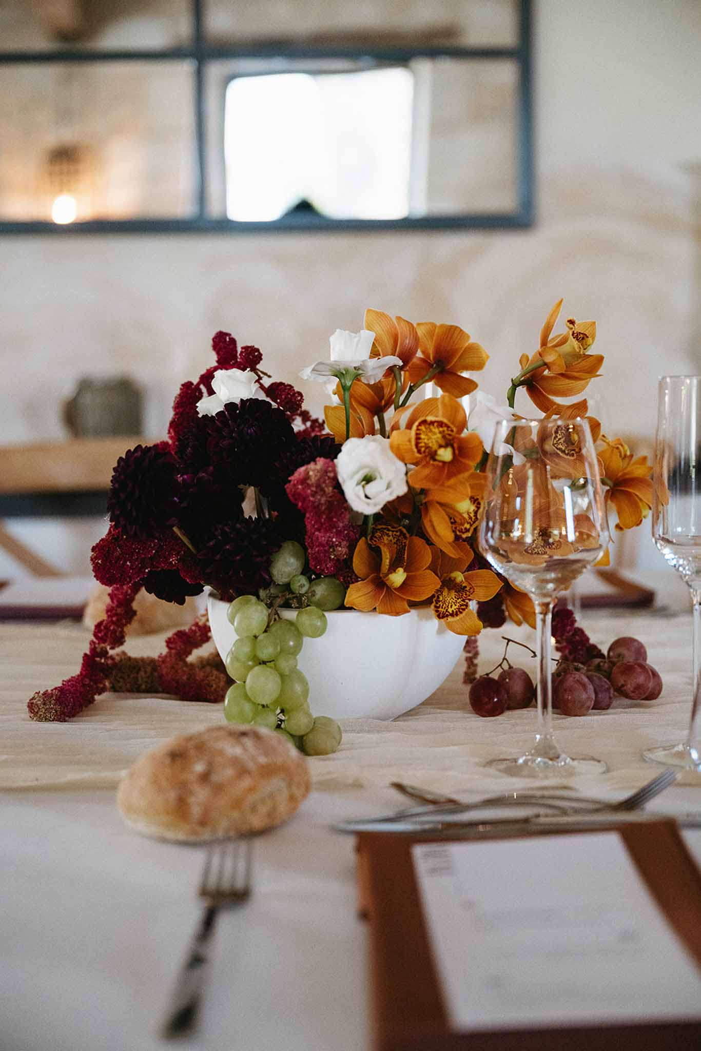 Autumn harvest centerpiece with burgundy dahlias, amber orchids, and grapes on linen tablecloth