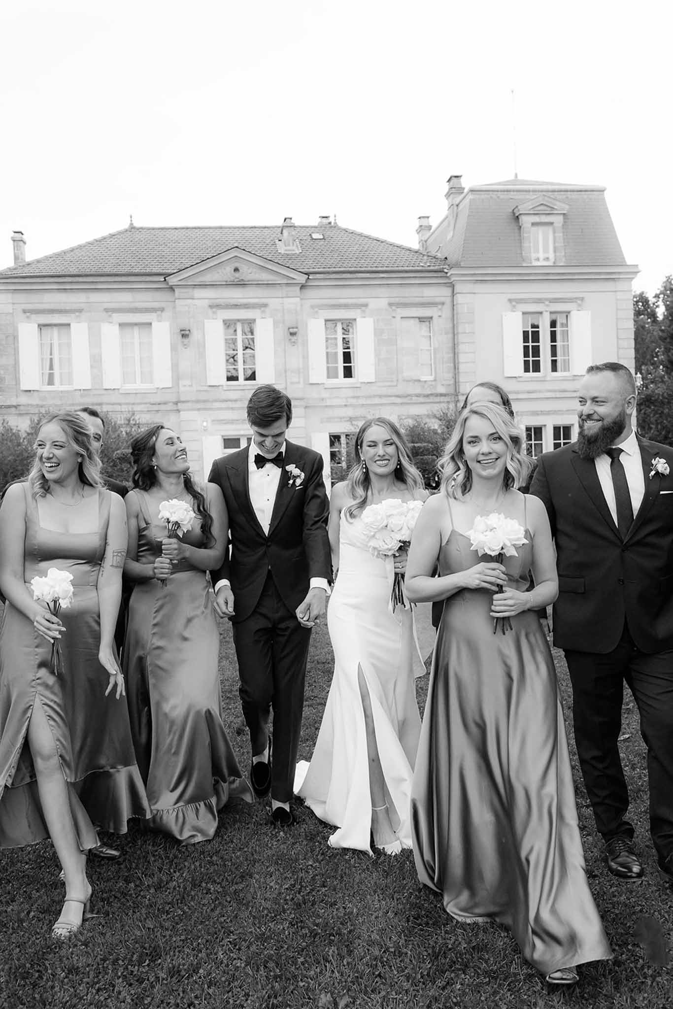 Wedding party walking across lawn in front of neoclassical mansion