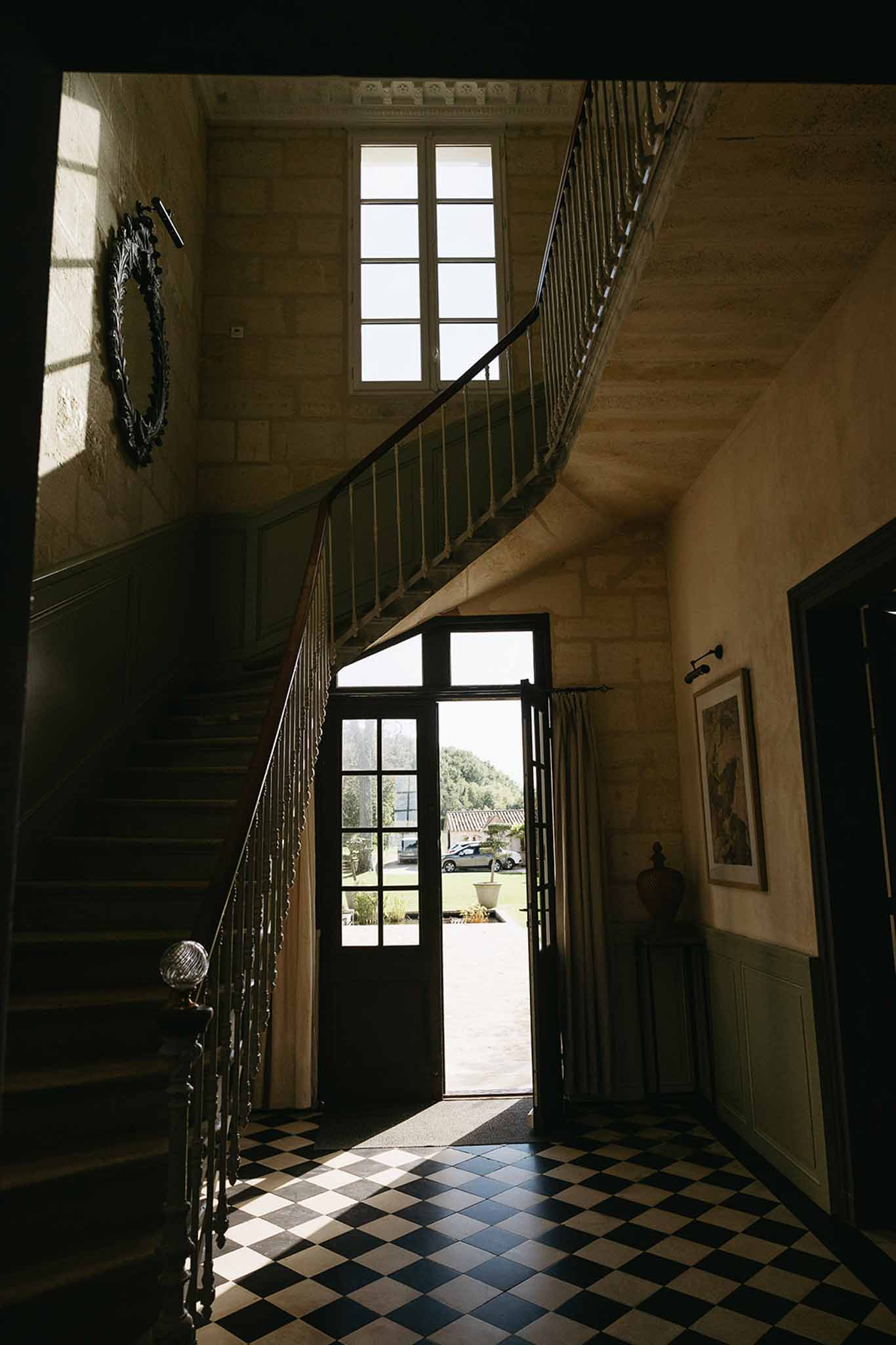 Grand chateau entrance hall with black and white tiled floor, curved staircase, wrought-iron balustrades, and tall windows