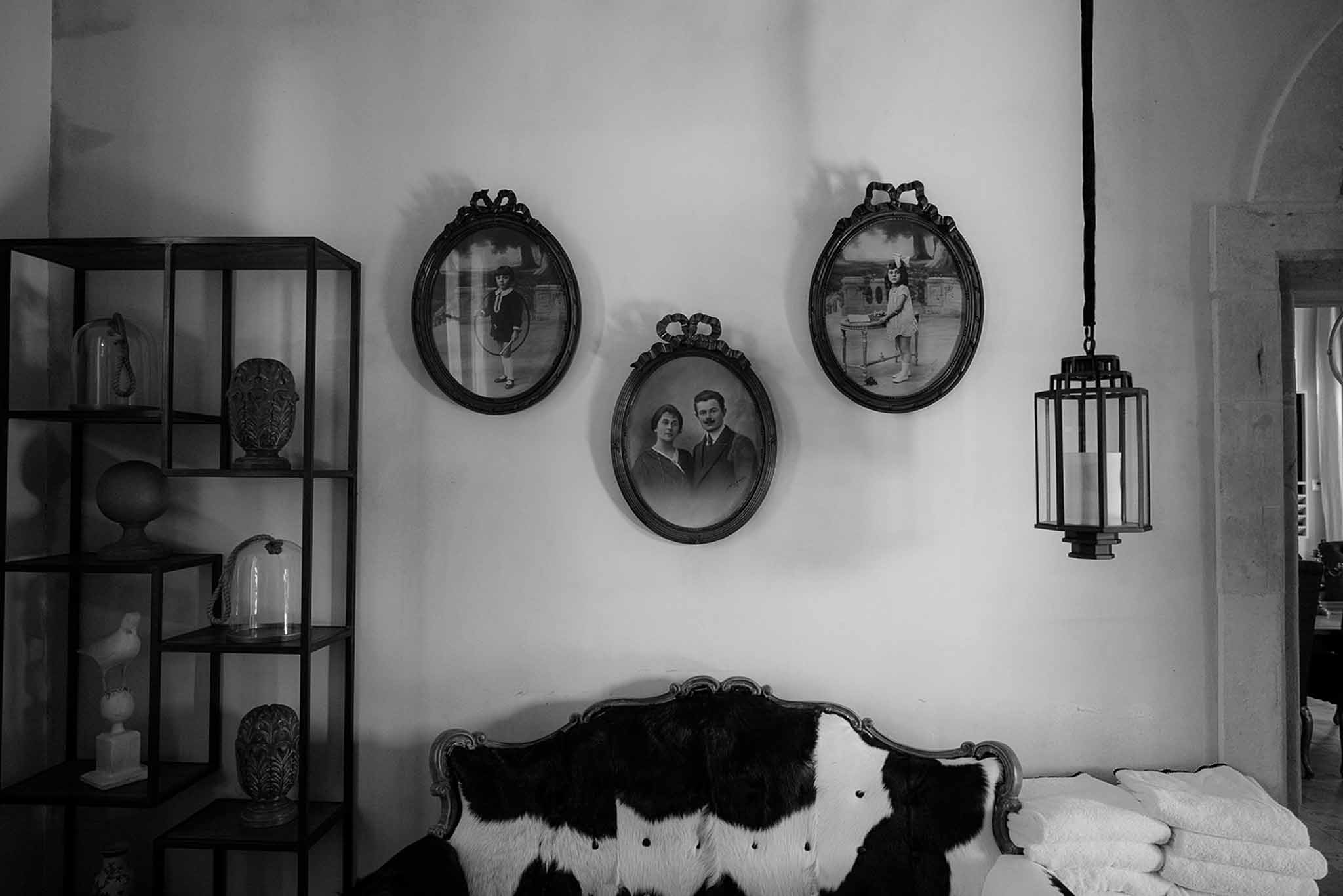 Black and white interior with oval-framed vintage portraits above cowhide sofa and antique curiosity shelving