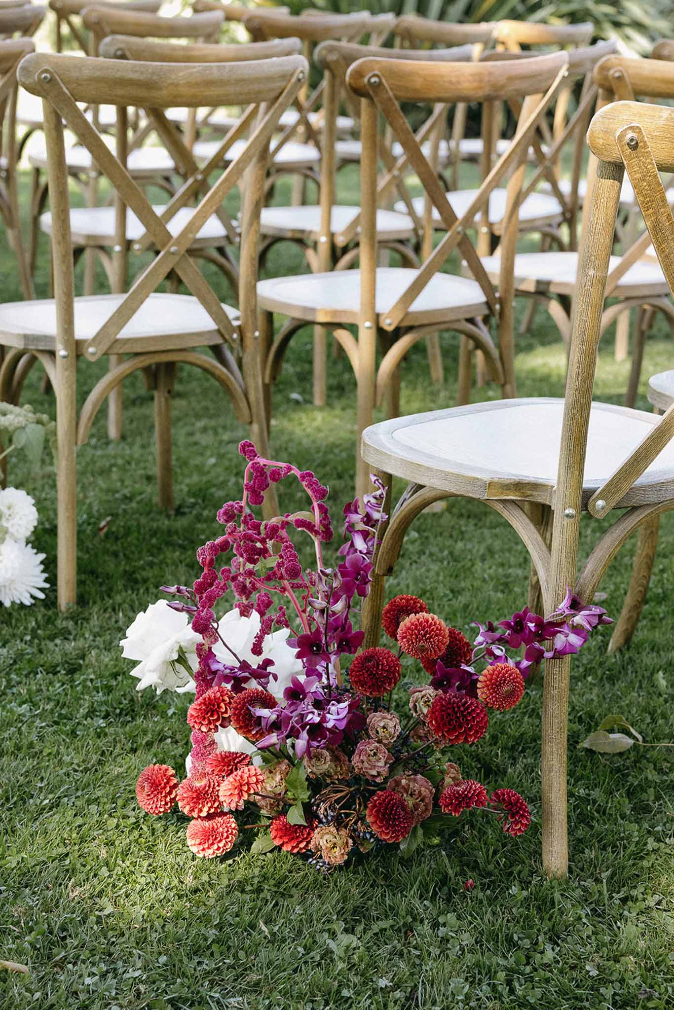 Ground-level autumn floral arrangement with orange dahlias and purple orchids beside ceremony chairs