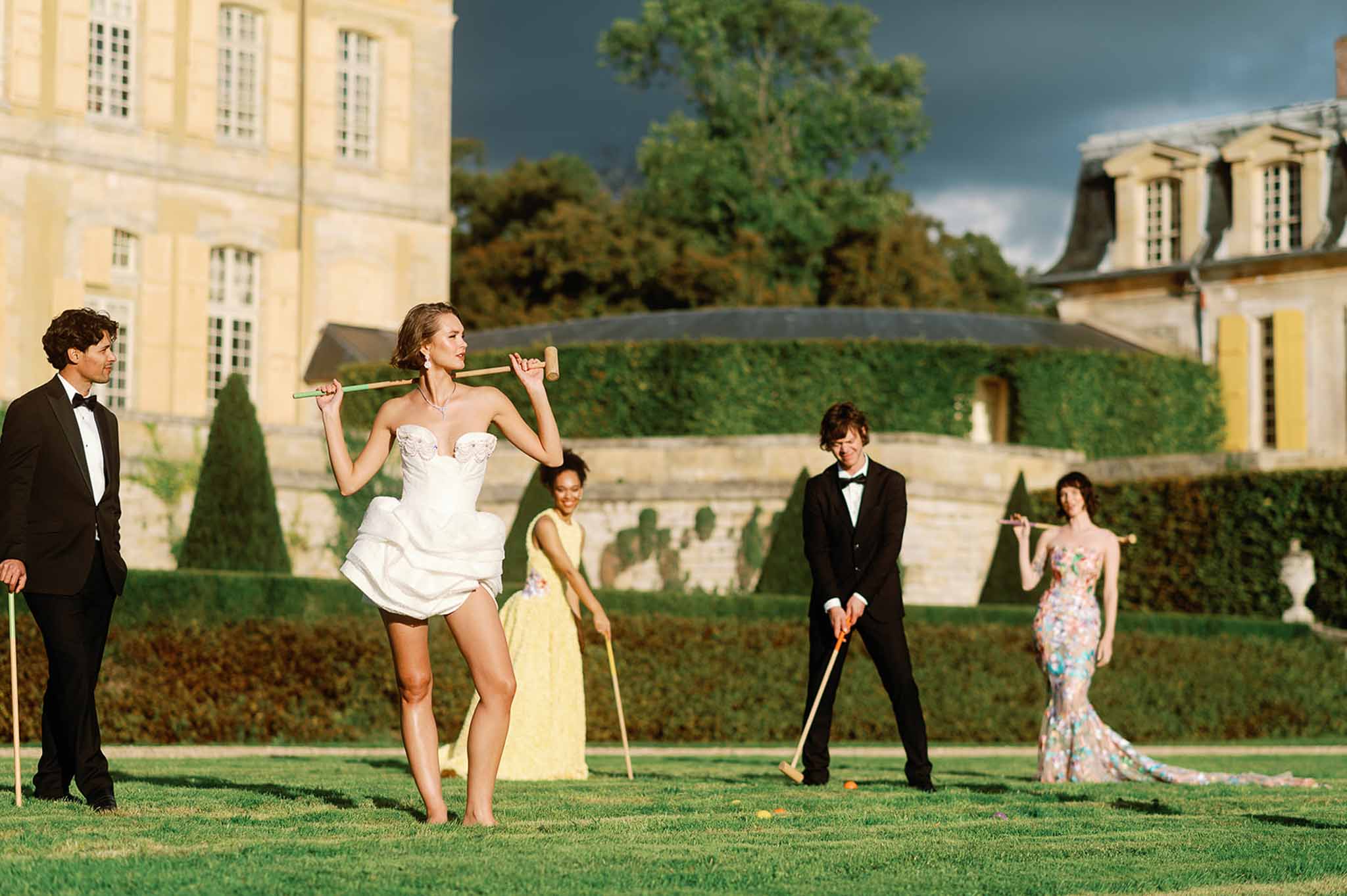 Bride and groom playing croquet with wedding guests in château garden courtyard
