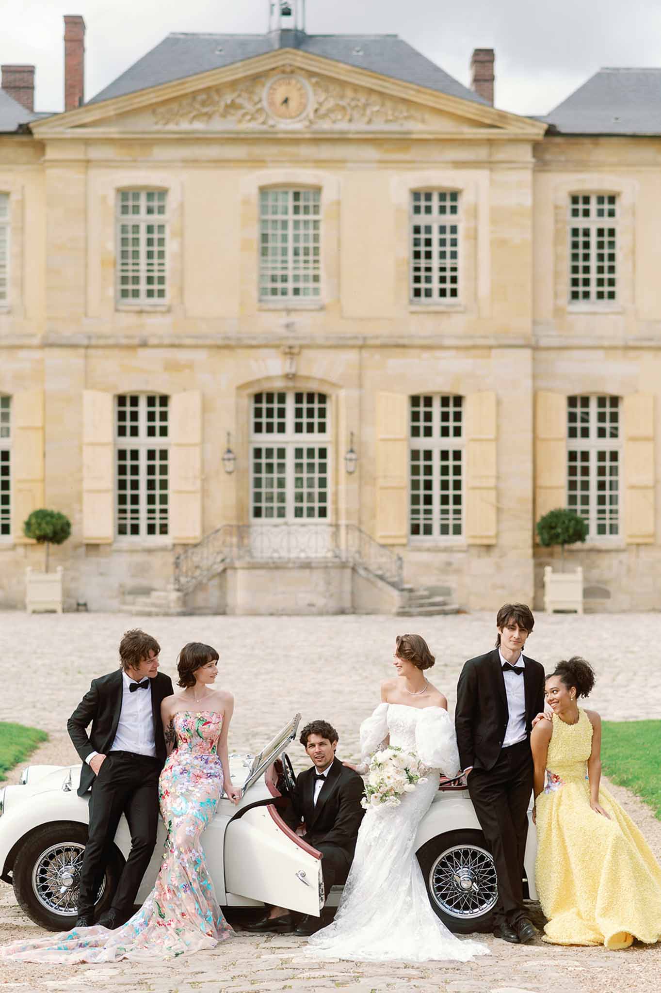 Bridal party with vintage convertible car in classical château courtyard