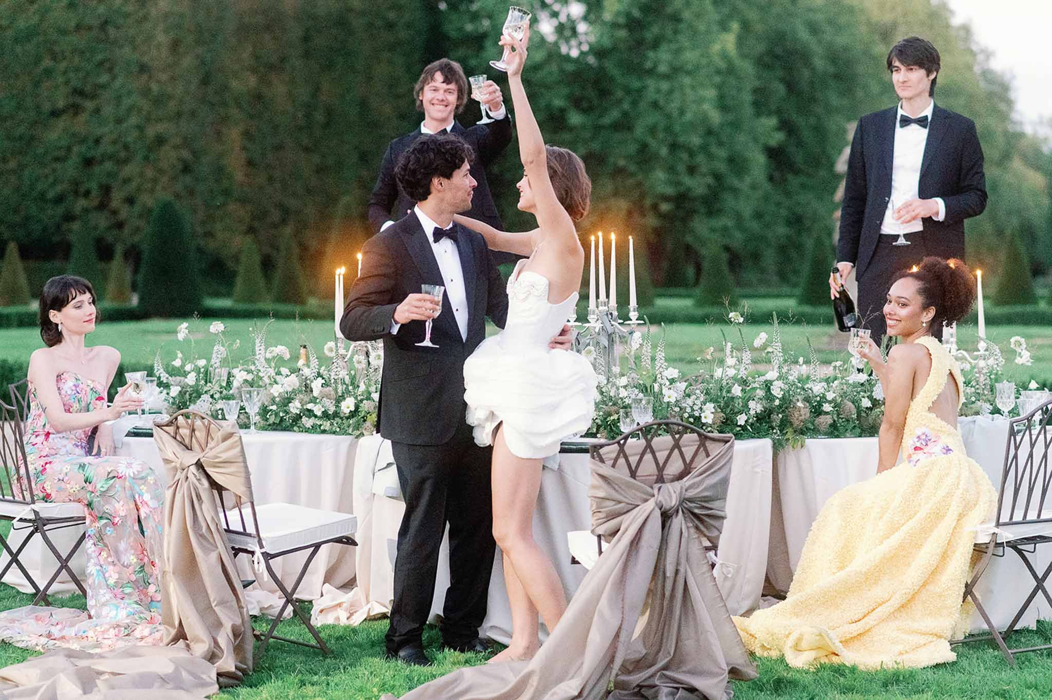 Bride and groom making toast during outdoor garden reception with guests at formal dinner tables