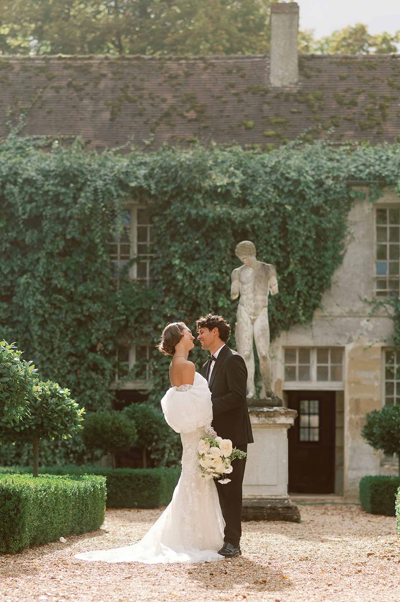 Bride and groom formal portrait in stone courtyard garden with classical statue and ivy-covered walls