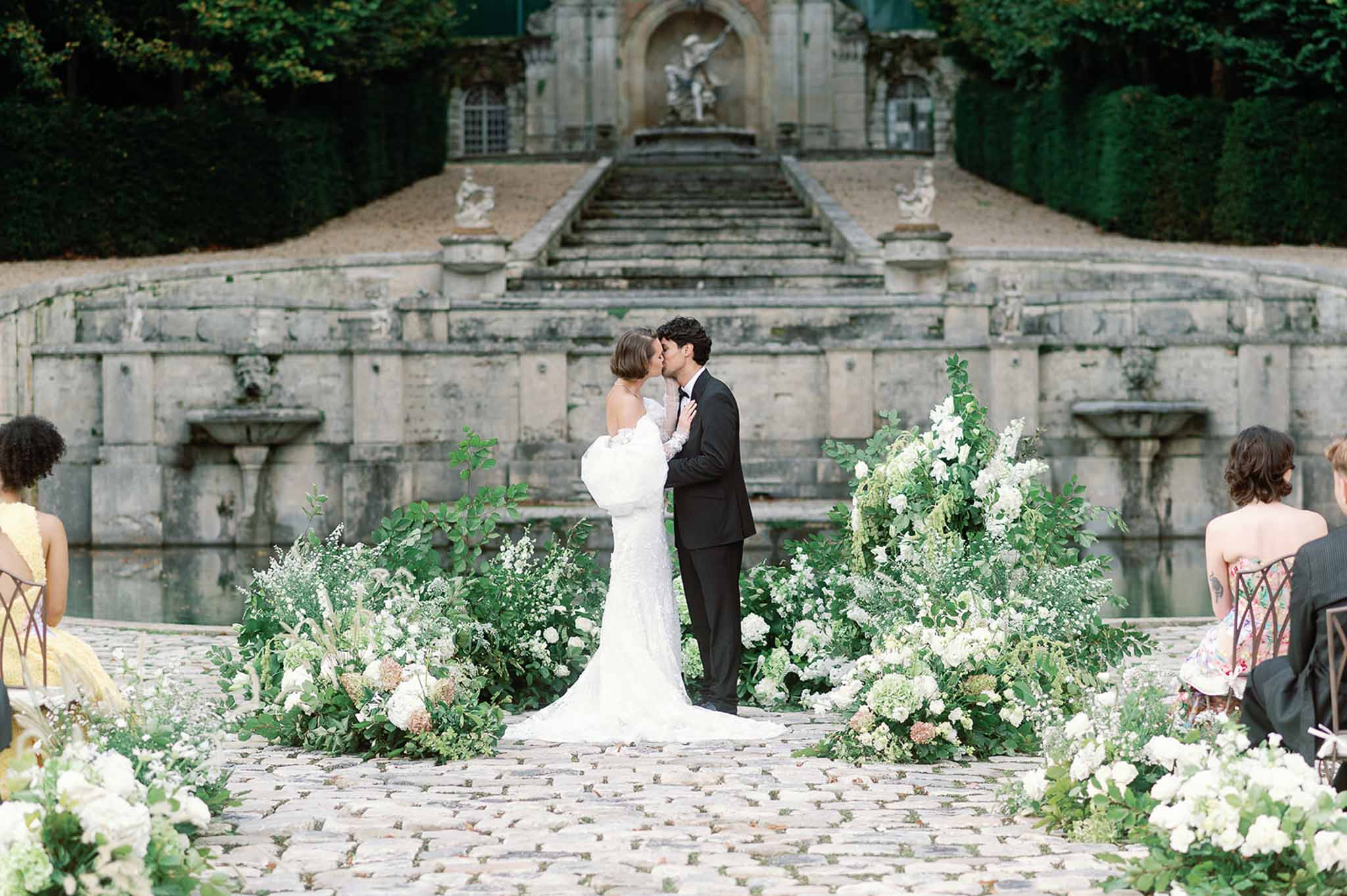 Bride and groom kissing during wedding ceremony in formal European garden courtyard with fountain
