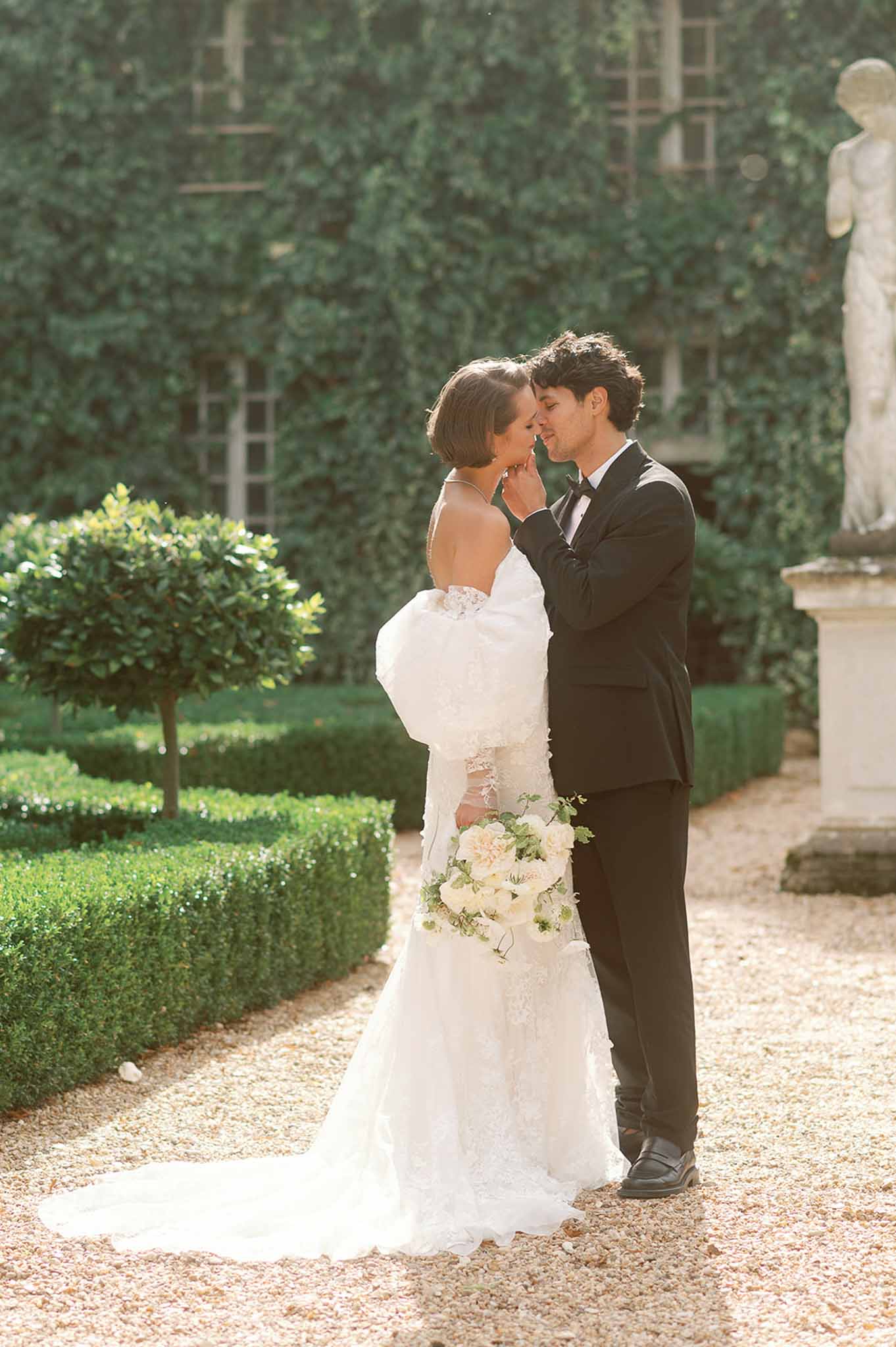 Bride and groom portrait session in formal garden courtyard with boxwood hedges and stone architecture