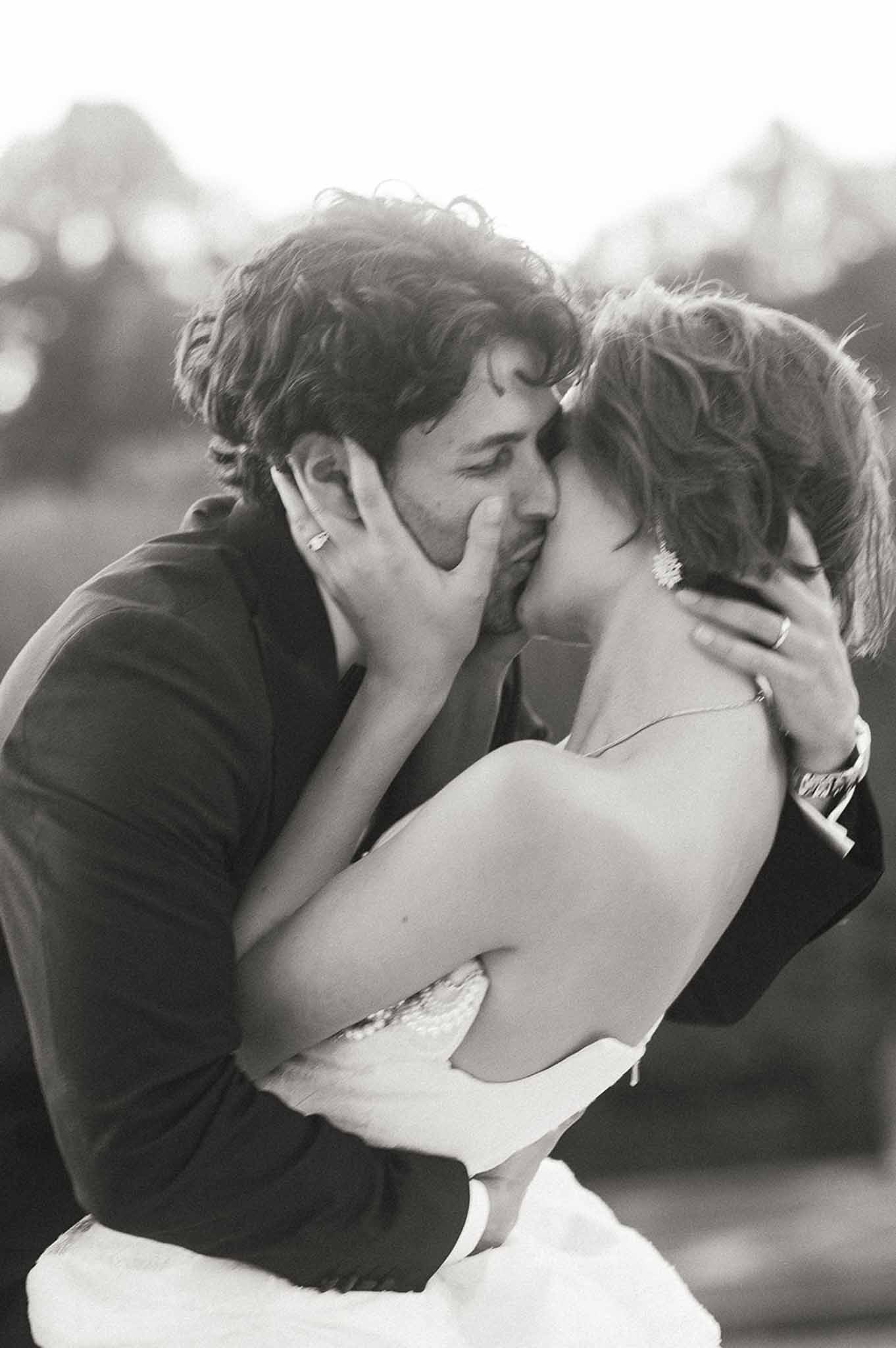 Black and white intimate portrait of bride and groom kissing outdoors with soft foliage background