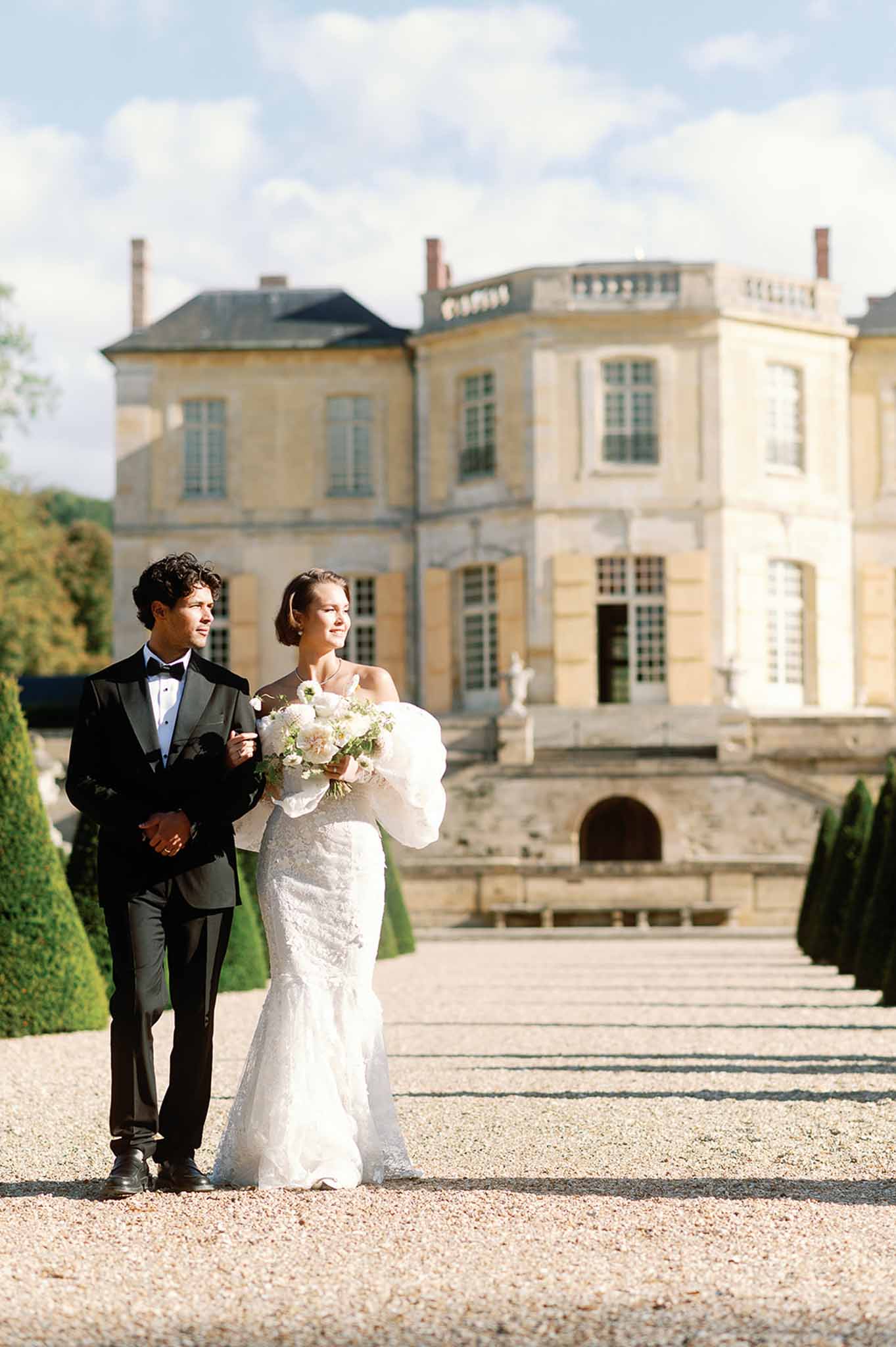 Bride and groom portrait in French château courtyard with classical architecture and manicured gardens
