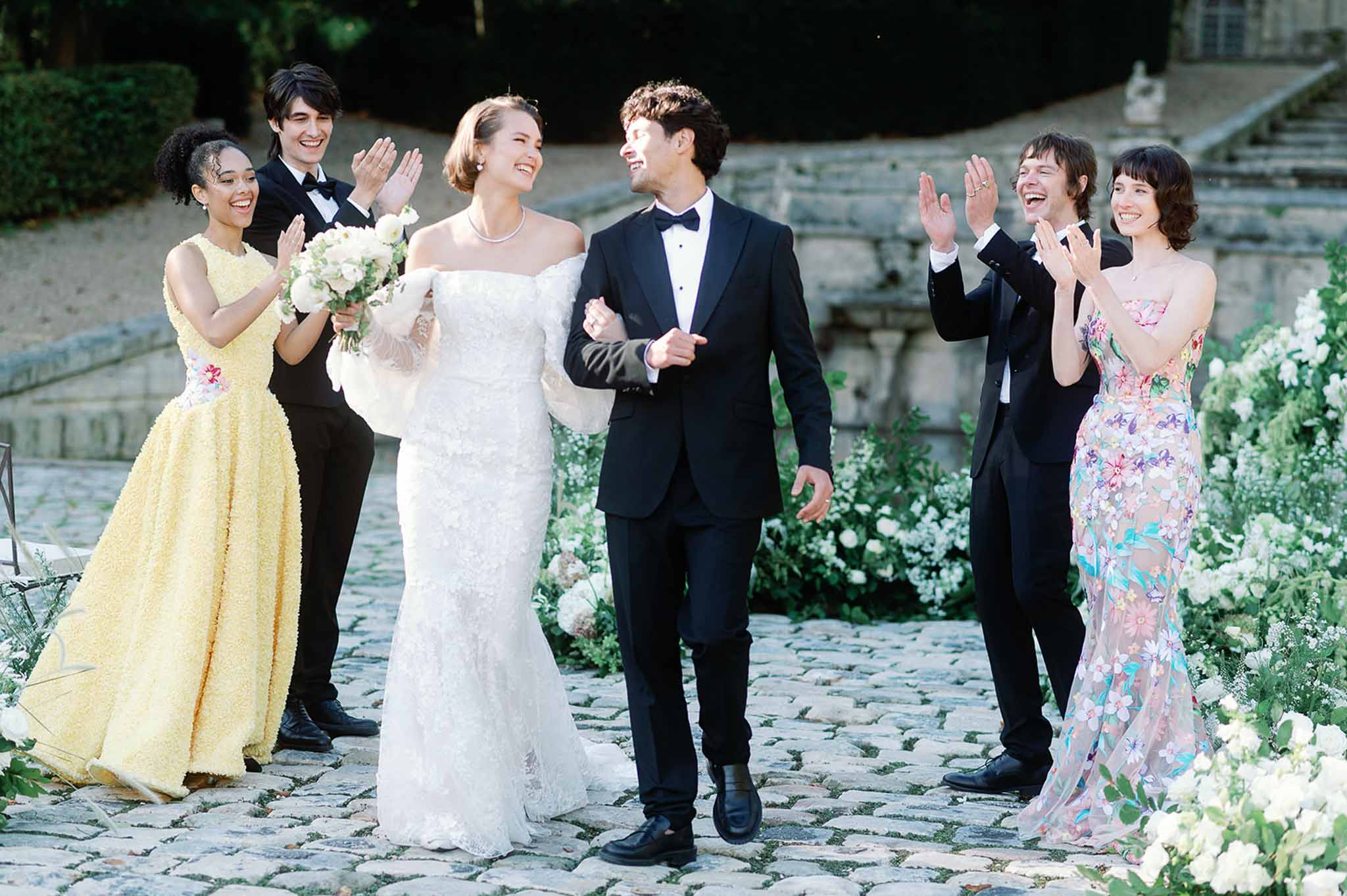 Bride and groom processional with wedding party in stone courtyard with garden florals