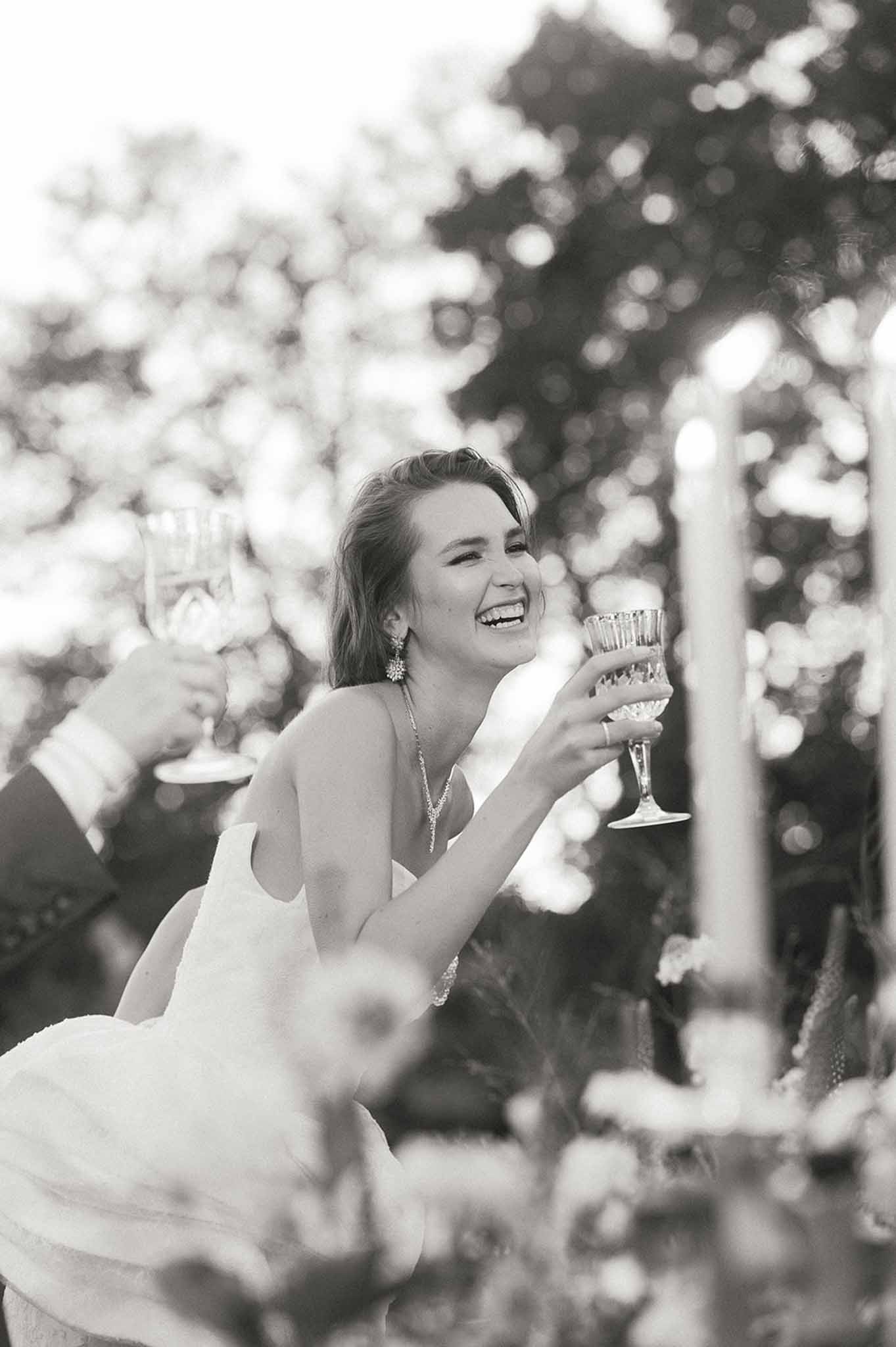 Bride laughing with champagne glass in garden setting during wedding celebration