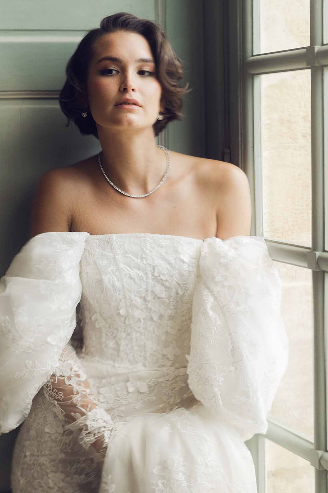 Bride in ivory lace gown posing by window in sage green paneled interior