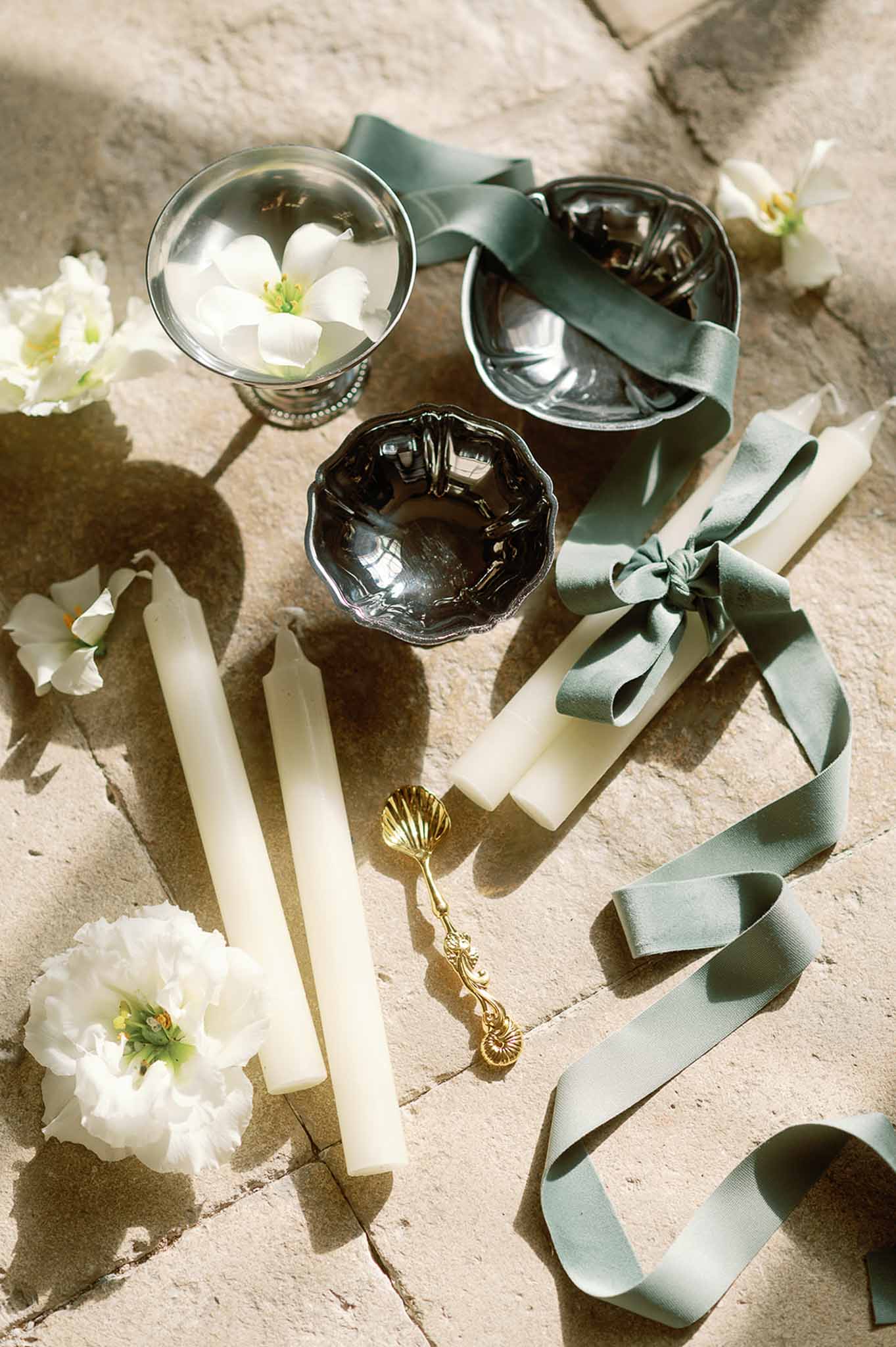 Wedding styling flat lay with candles, ribbons, and flowers on stone surface
