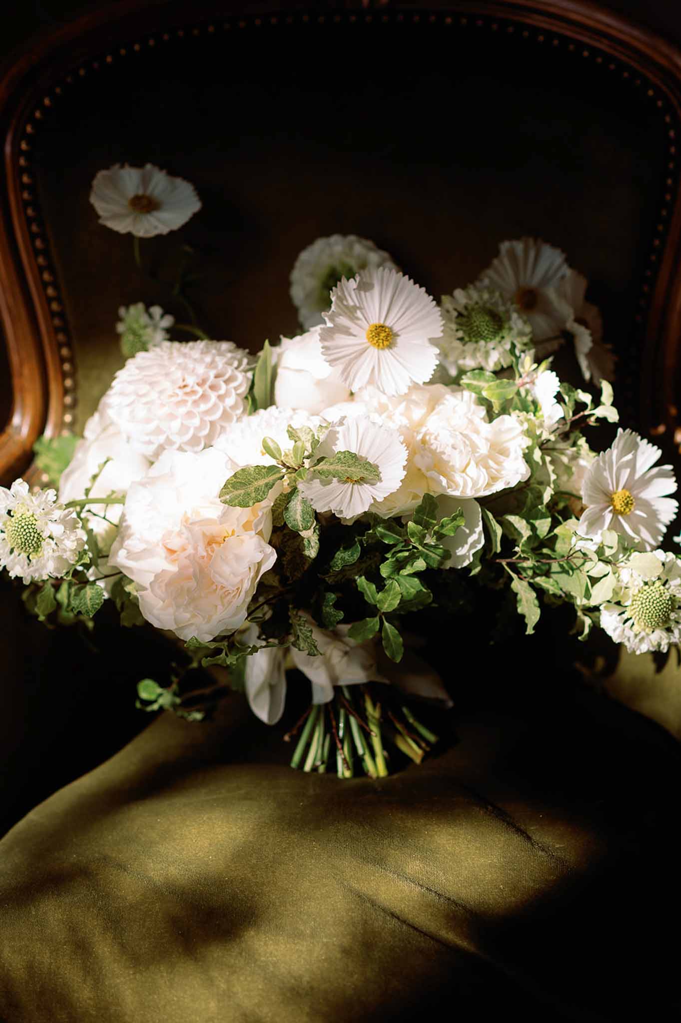 Bridal bouquet with cream roses and sage foliage on olive fabric background