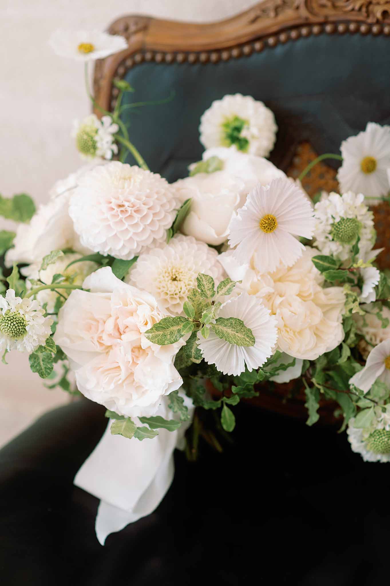 Bridal bouquet with cream dahlias and white roses on ornate wooden chair