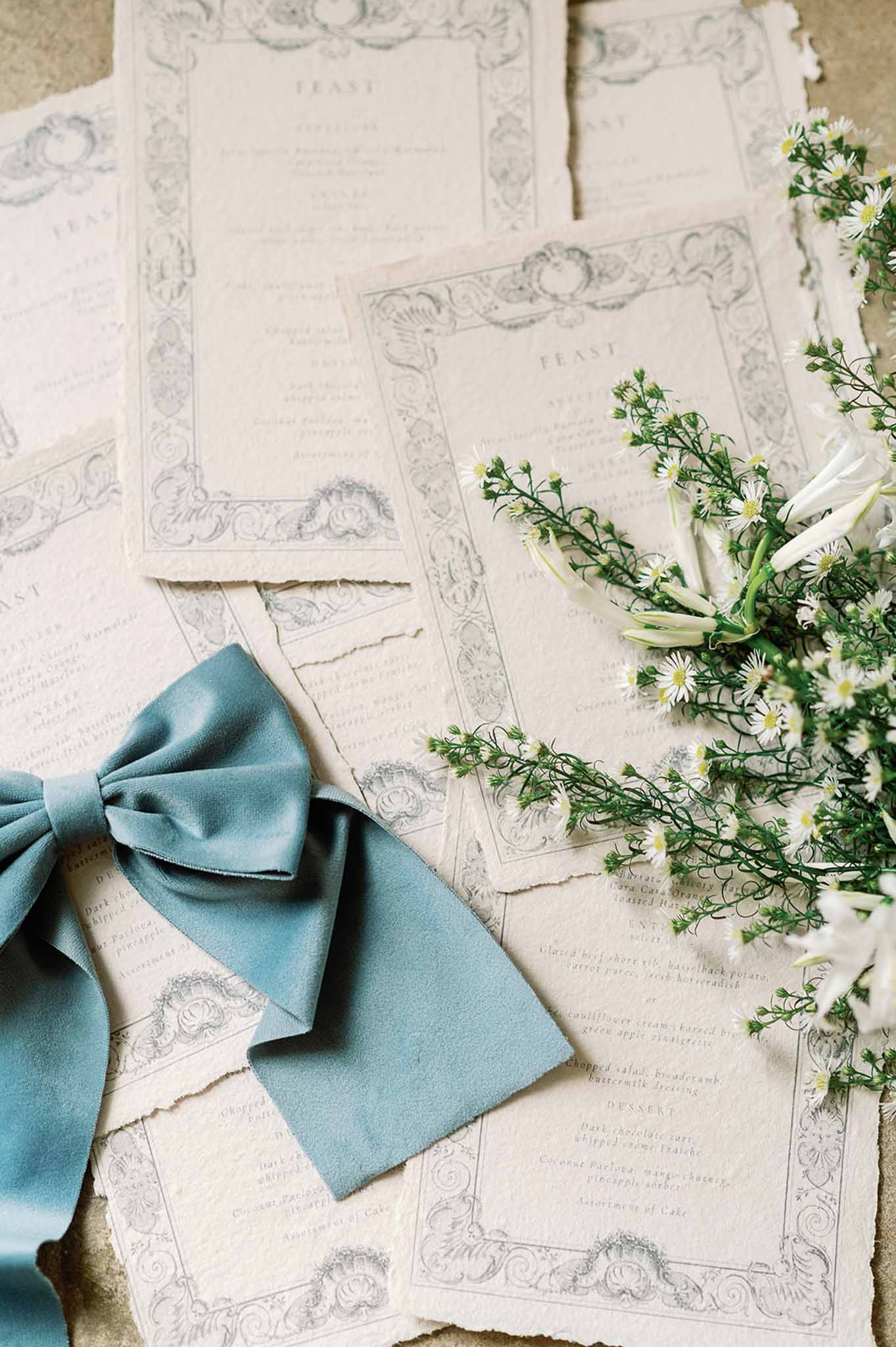 Wedding menu cards with dusty blue ribbon and white flowers flat lay arrangement