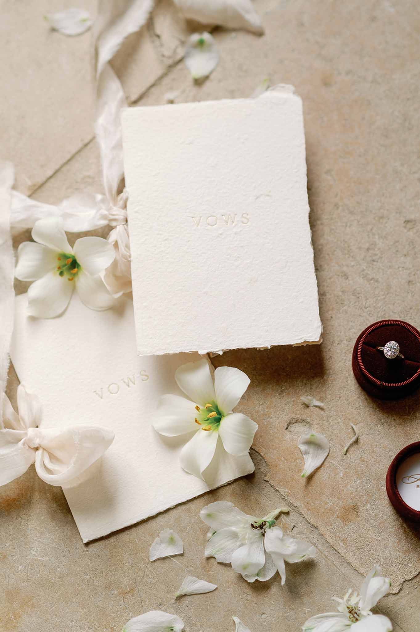 Wedding vow booklets with engagement ring and white flowers arranged on beige surface