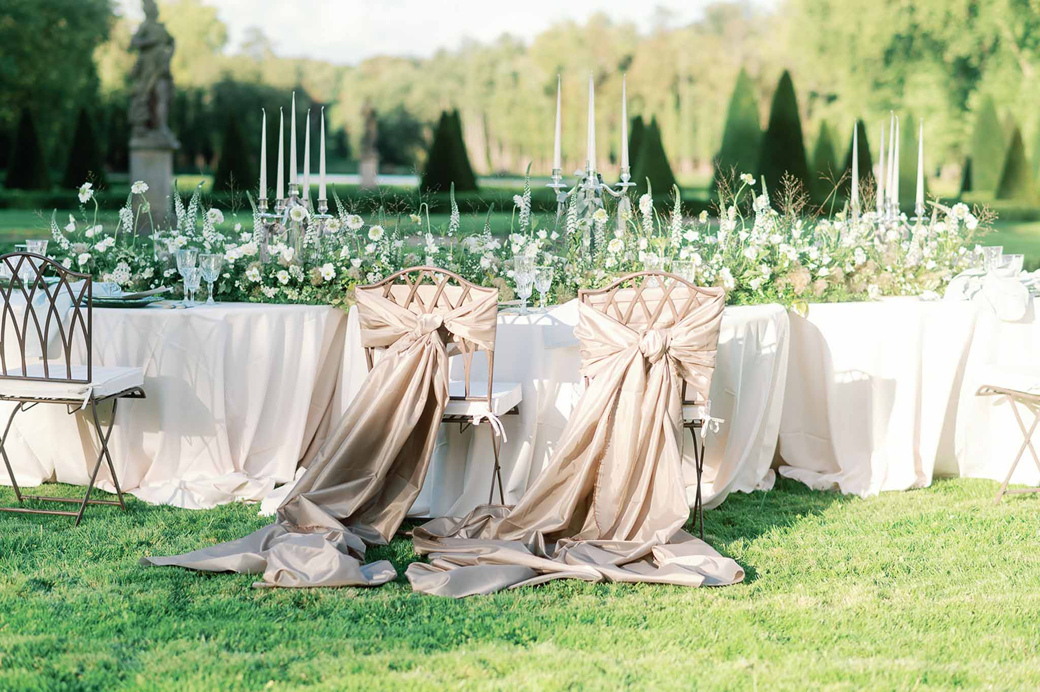 Outdoor wedding reception table settings with white florals and candelabras in formal garden