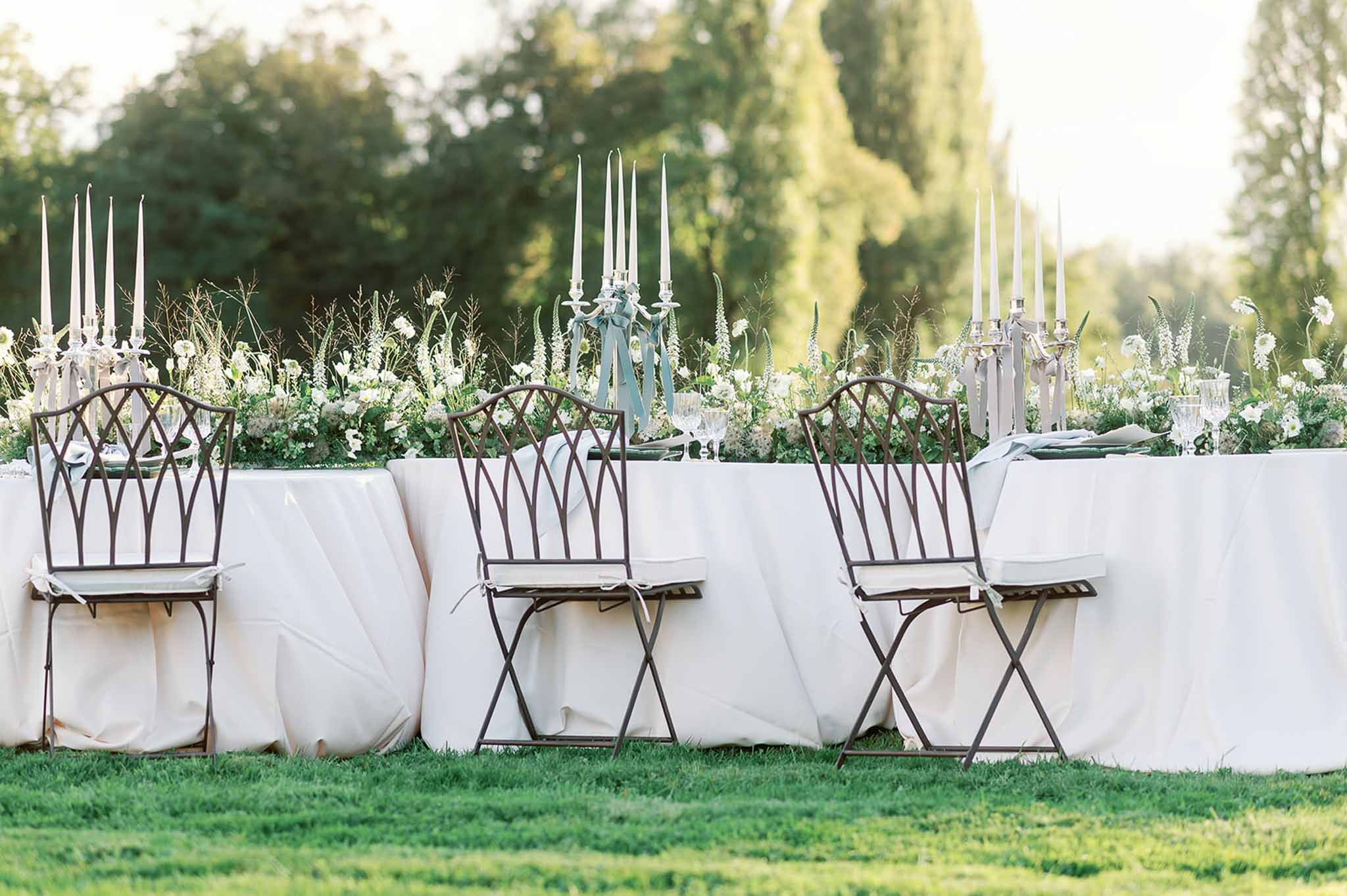 Elegant outdoor reception table with silver candelabras and white florals in manicured garden setting