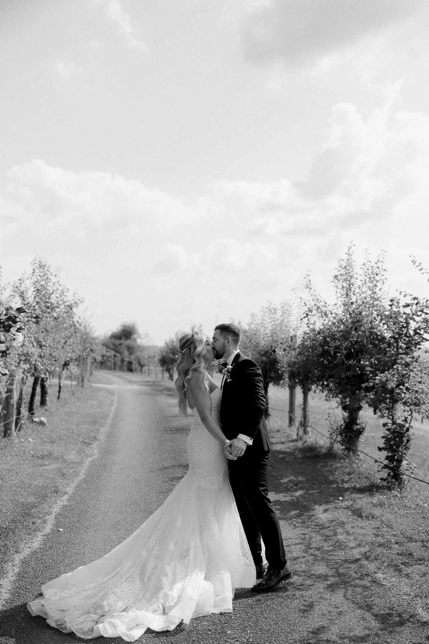 Bride and groom holding hands on tree-lined rural road in black and white wedding portrait