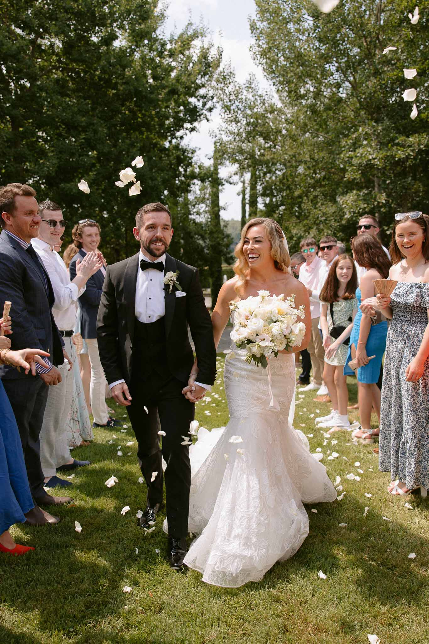 Bride and groom walking down outdoor aisle after ceremony with guests throwing petals in garden setting