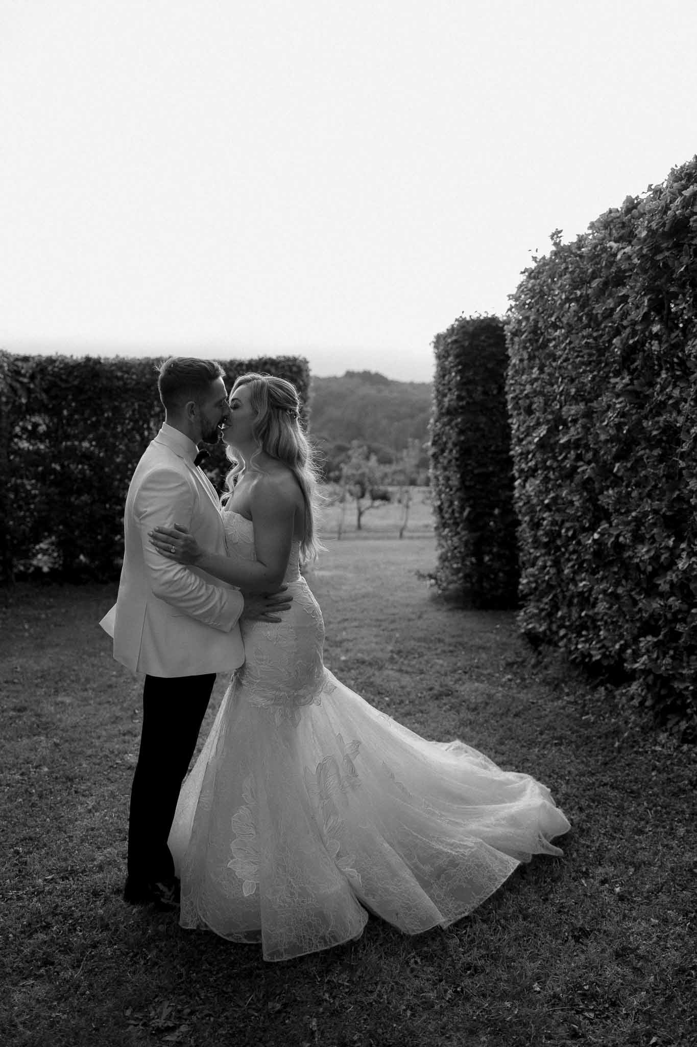 Bride and groom kissing in formal garden corridor with sculpted hedges