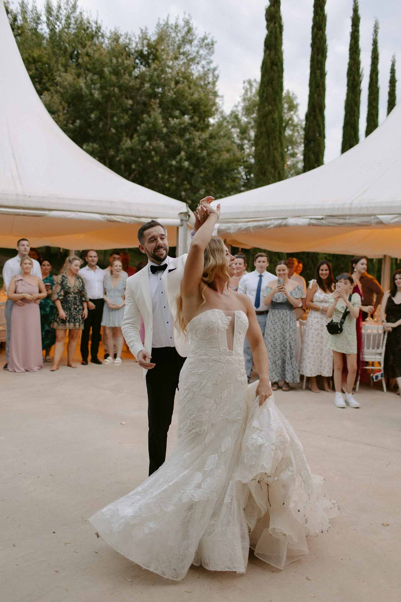 Groom spinning bride during first dance under white sail canopy surrounded by watching guests