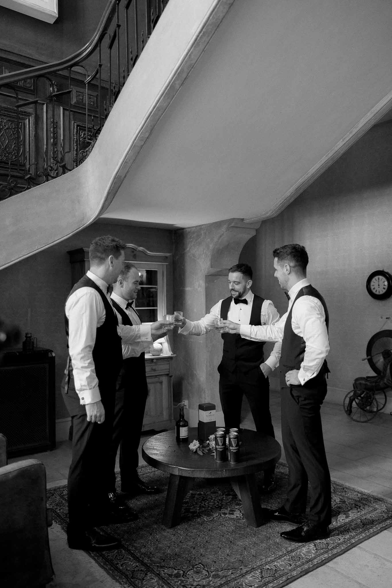 Groom and groomsmen toasting with champagne glasses in modern interior space during wedding preparation